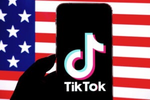 Photo illustration of the TikTok logo displayed on a phone screen with an American flag in the background.