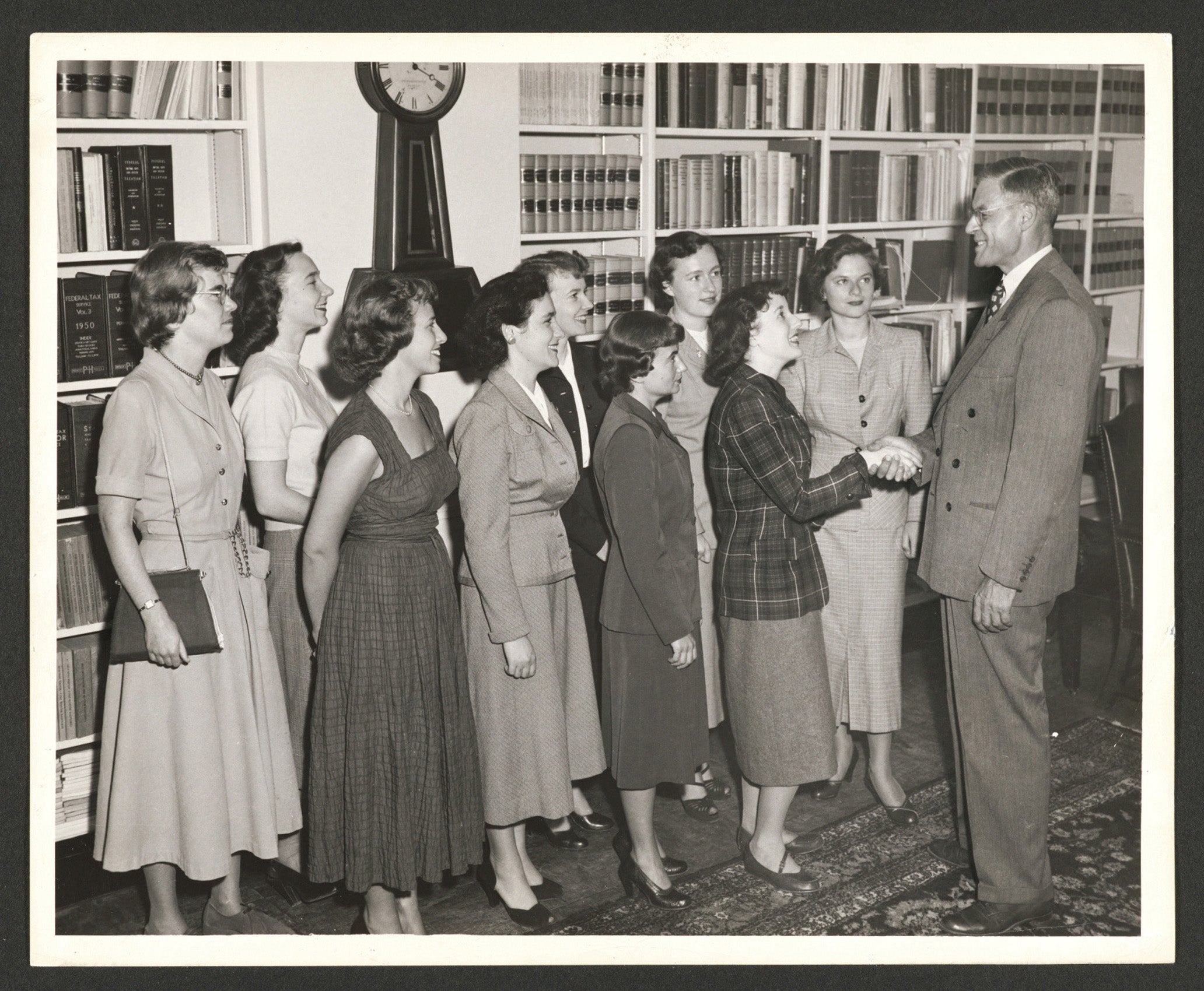 Nine women standing in two lines in a library greeting meeting with a gentleman