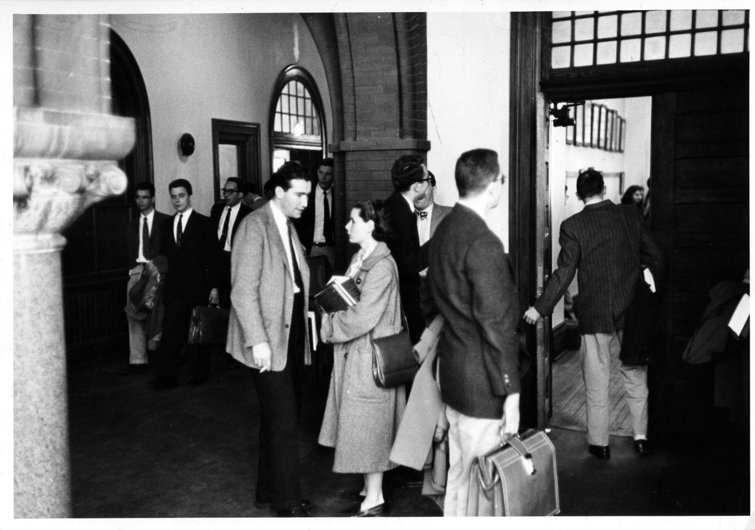 Male students in suit and tie and one woman in the hallway outside a classroom