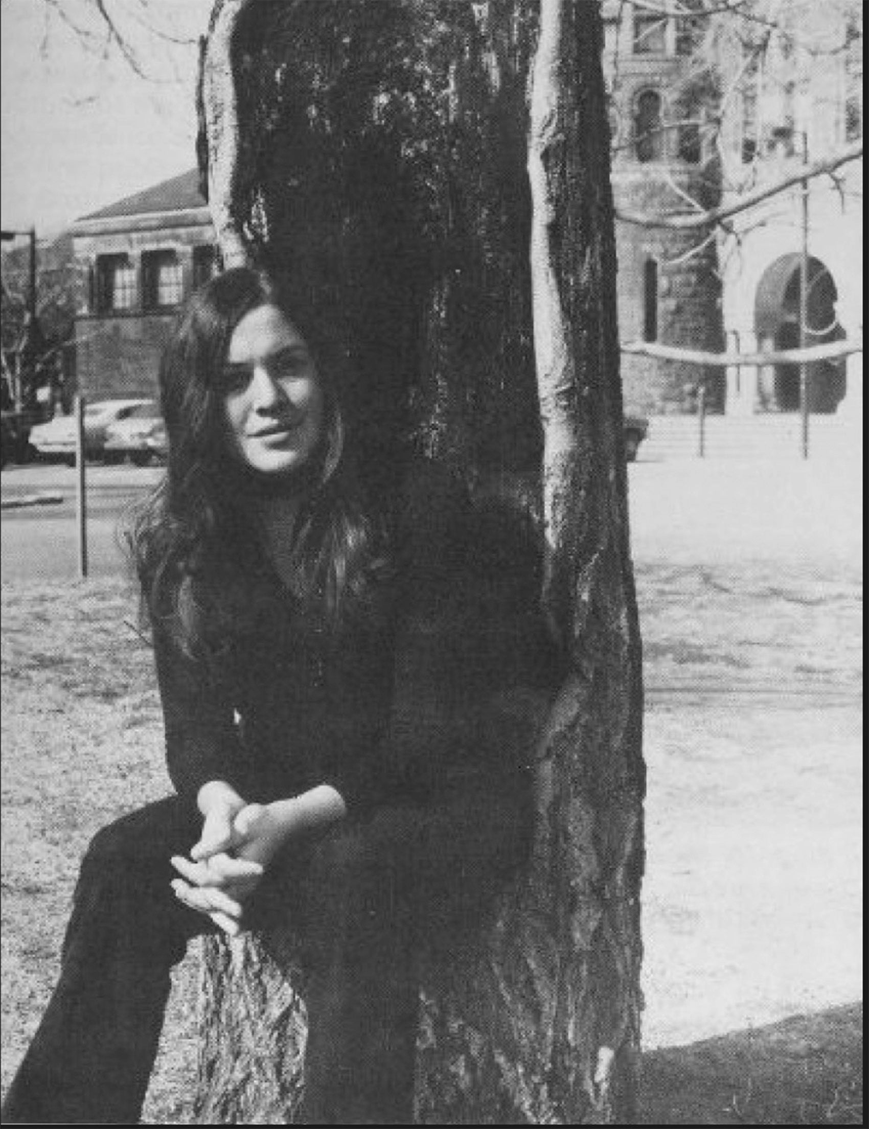 A portrait of a woman sitting on the stump of a tree on campus