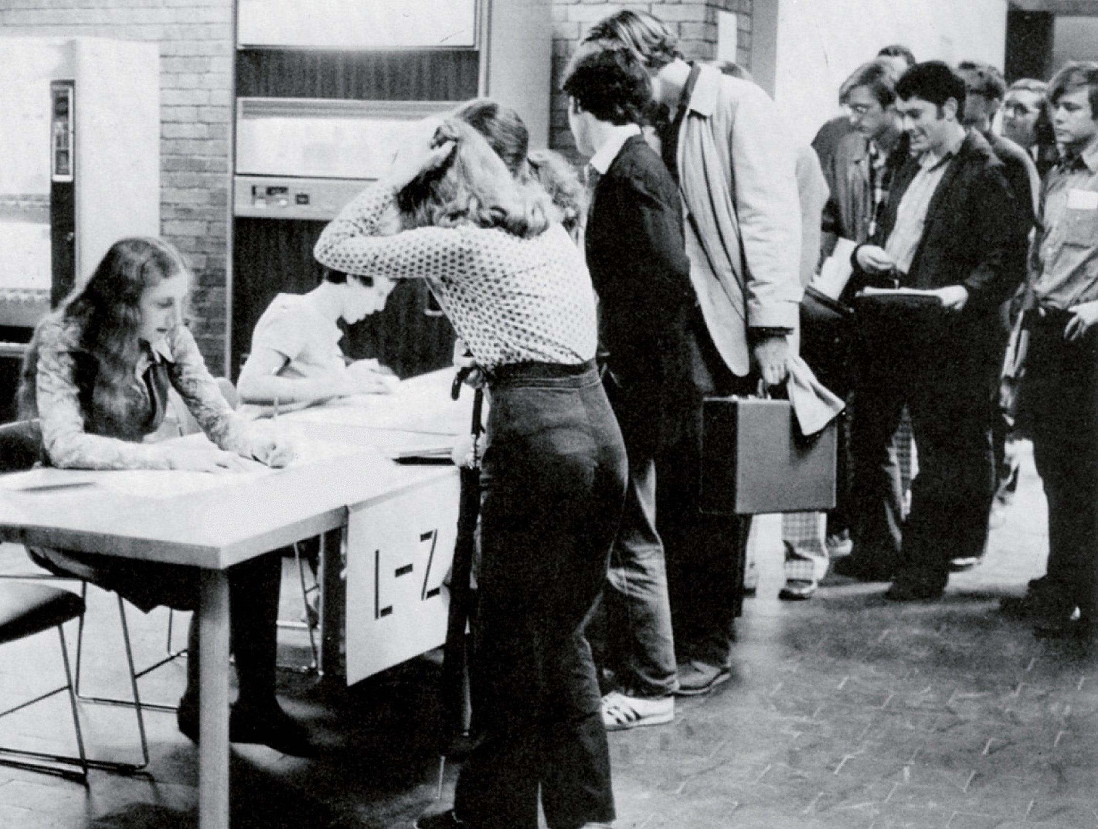 A women in a registration line hold her hands on her head as she talks with someone getting her set up