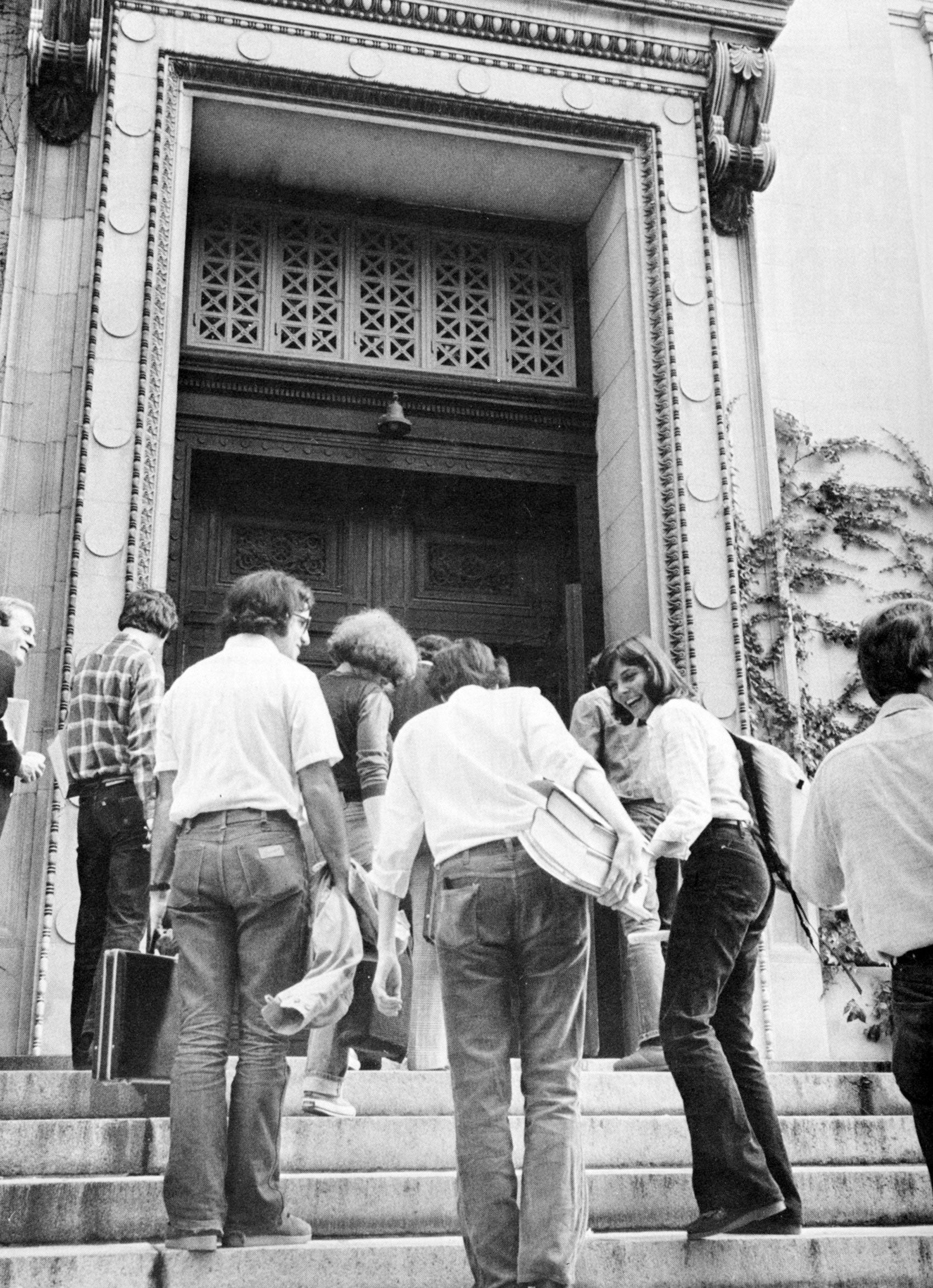 A group of men and one woman head to class up a set of stairs with briefcases and books
