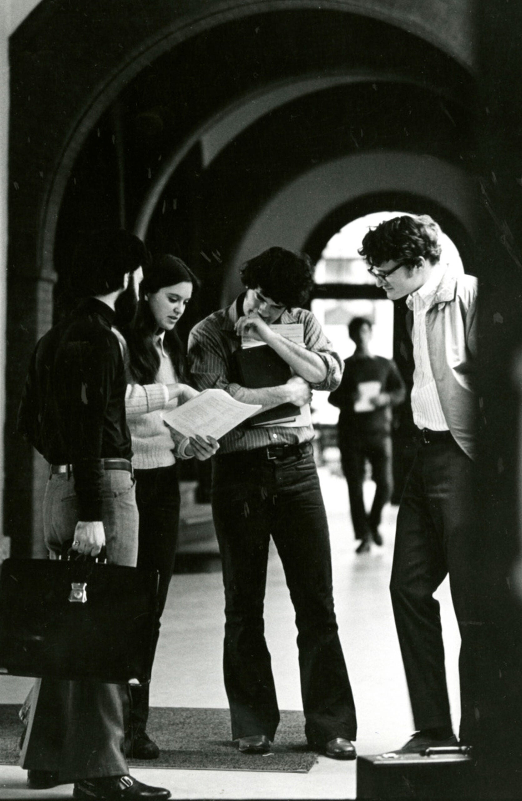 Three male students converse with a woman student about a piece of paper in her handin the hallway of Austin Hall