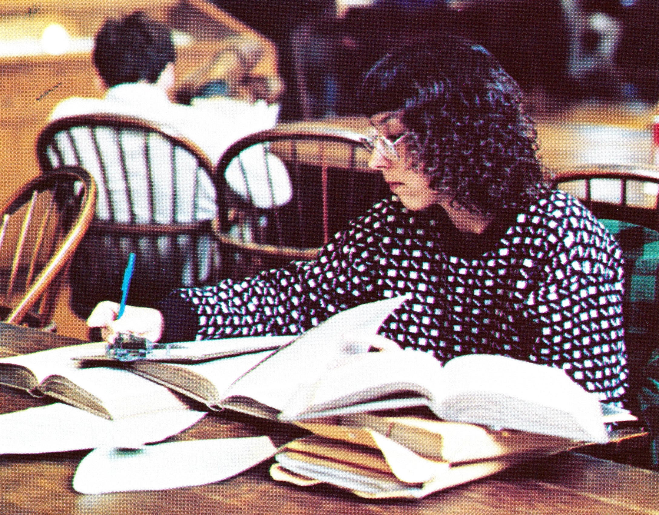 A women sitting at a table in the library with a pile of open books taking notes