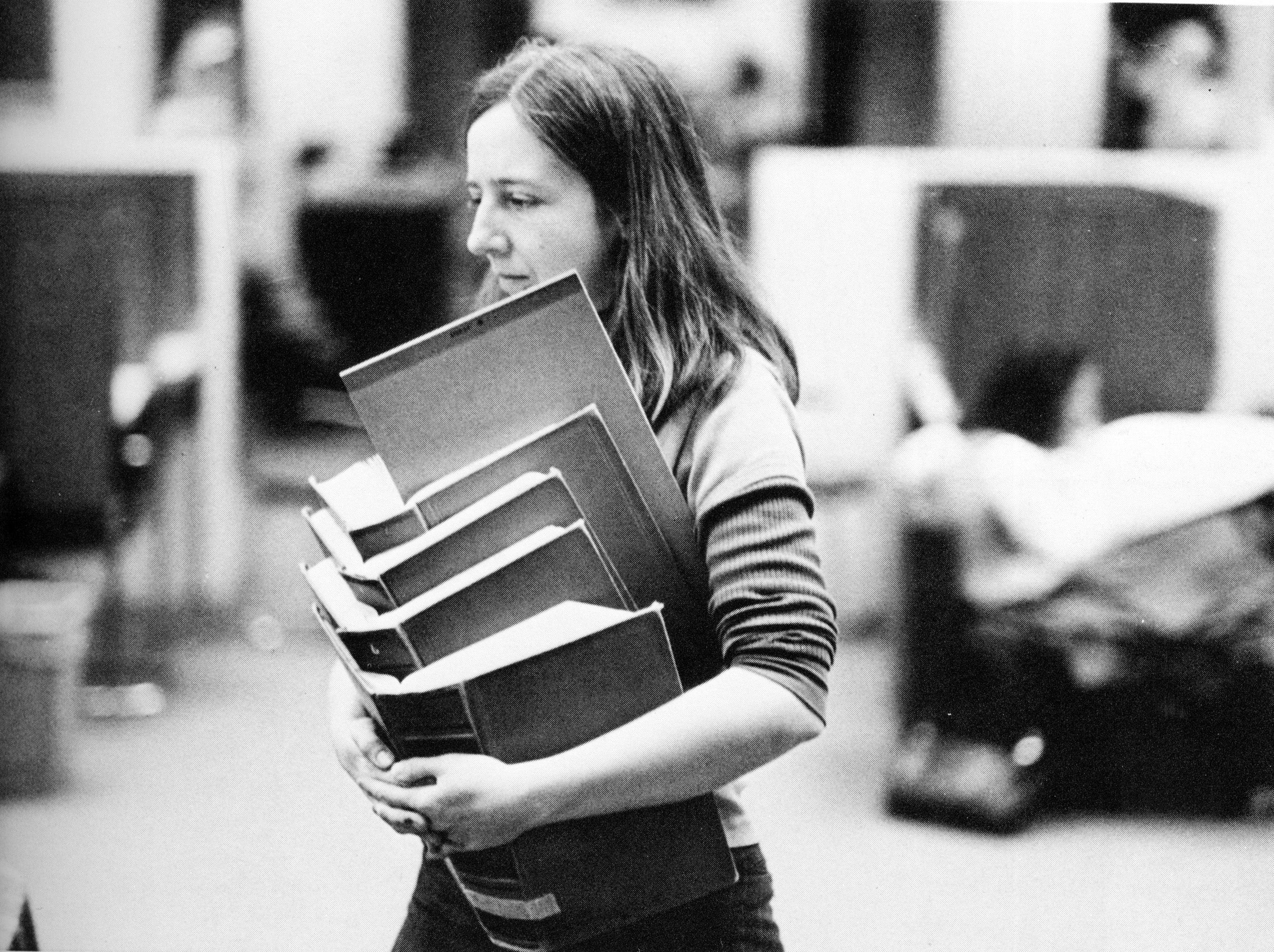 A woman carrying a pile of 5 heavy law books