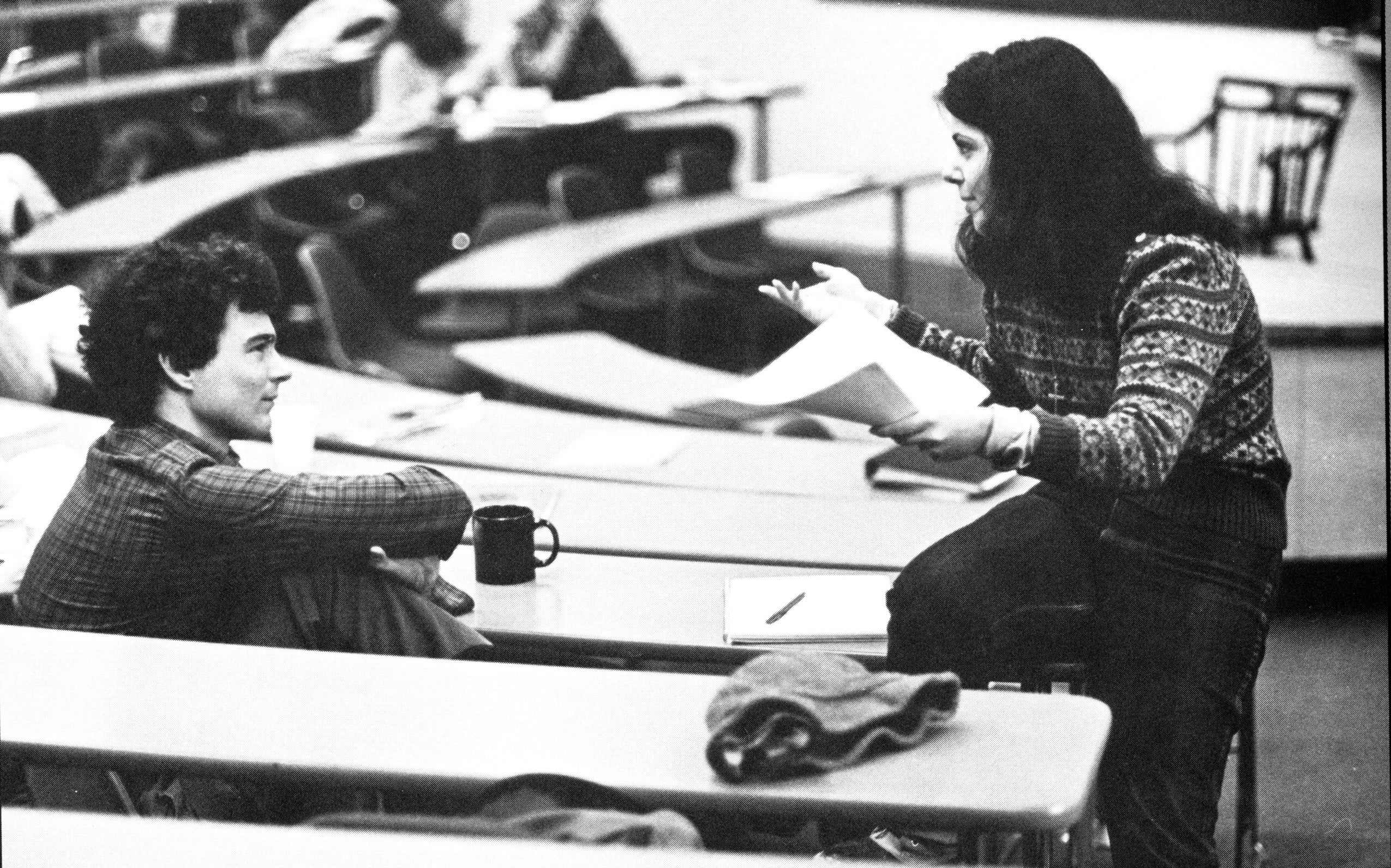 In a classroom a woman talks to a male student.