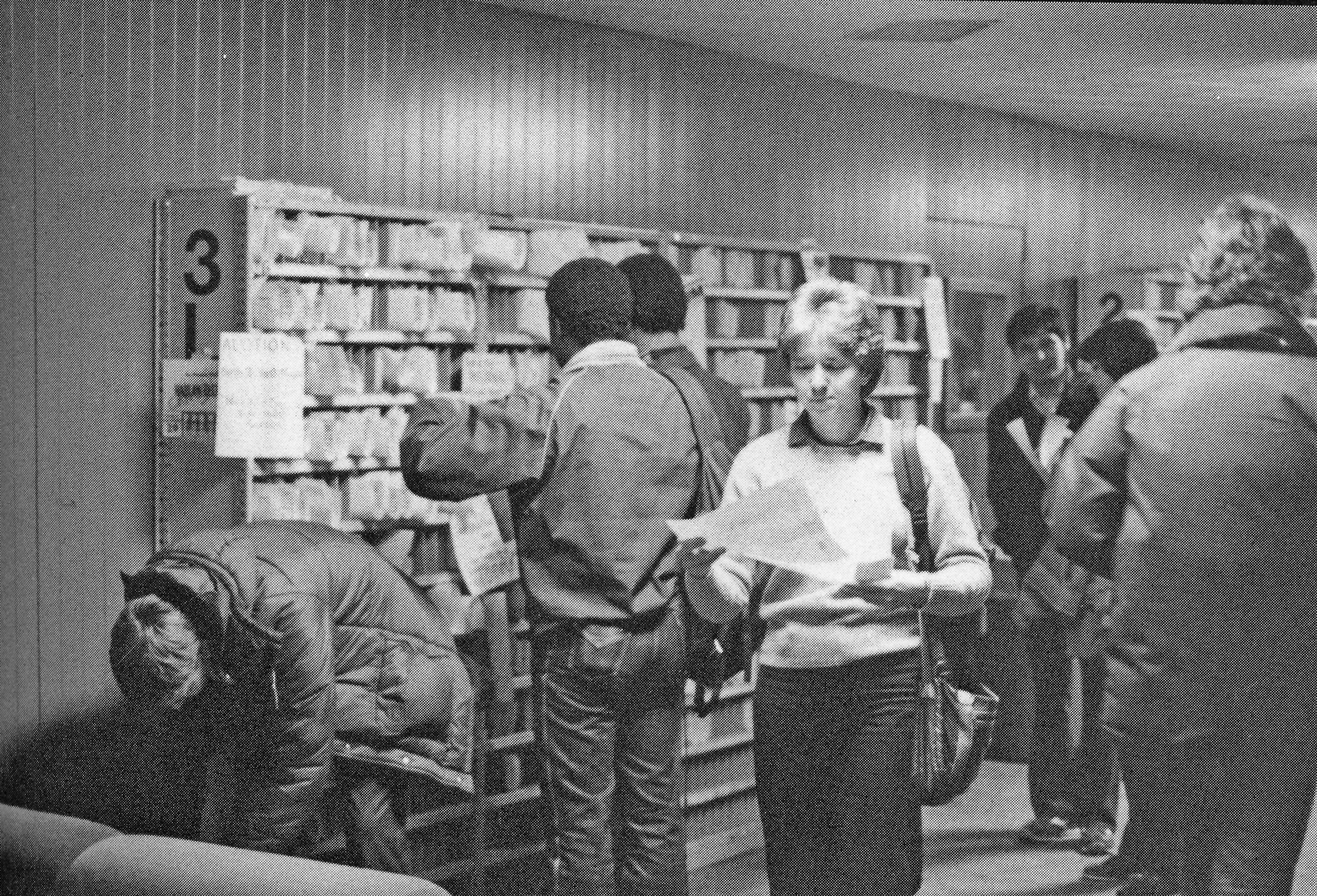 Students checking mailboxes filled with papers one female student walks away holding a piece of paper