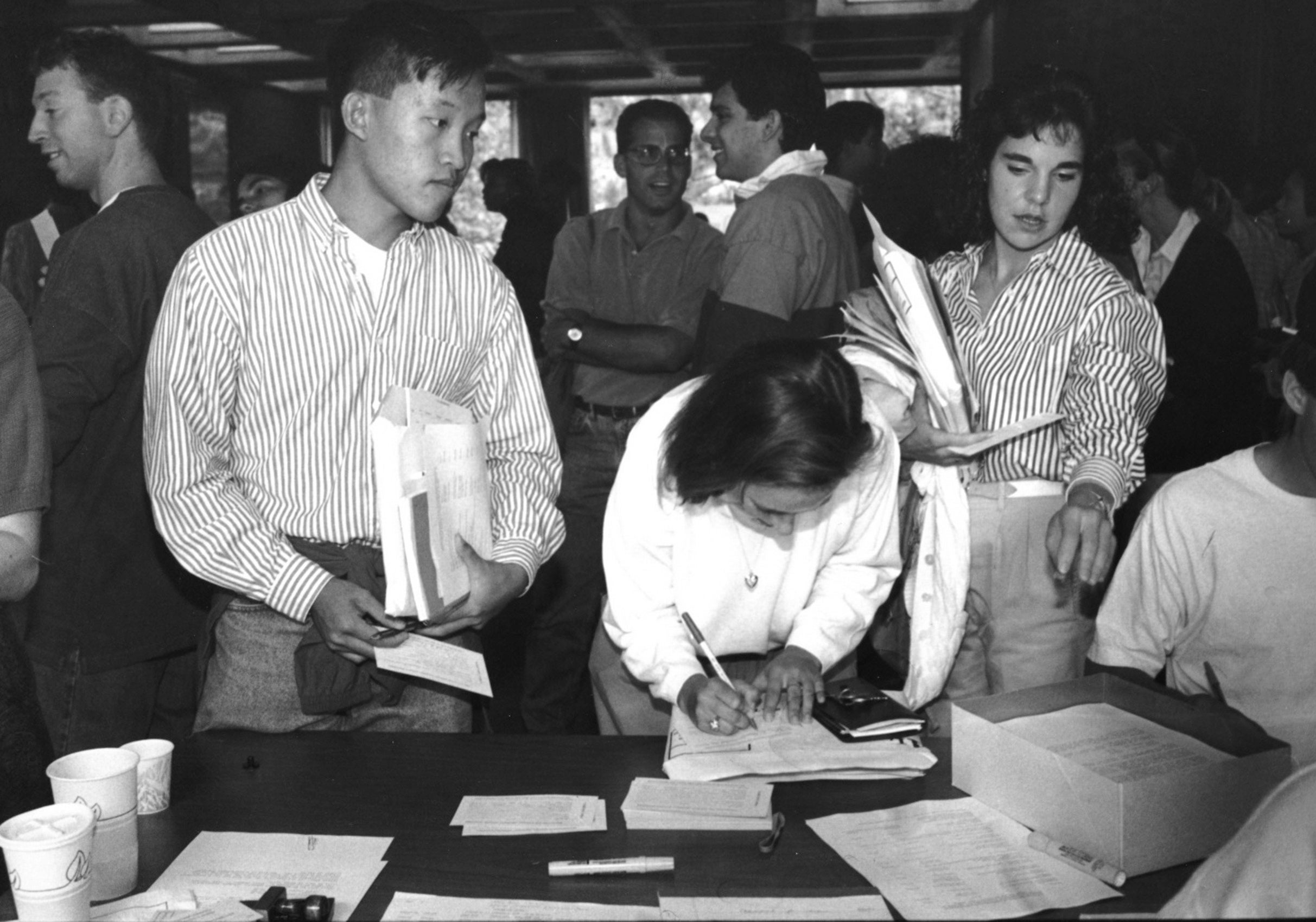 A women points to something on a table as she registers and other students are nearby