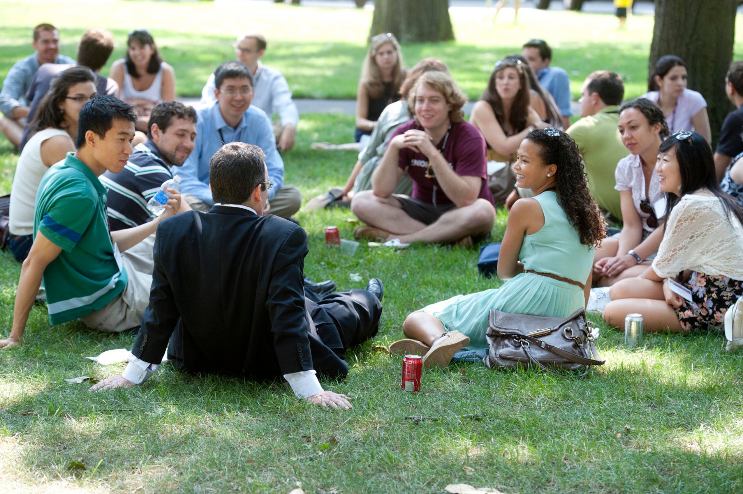 Groups of students talk as they sit in circles on a grassy lawn
