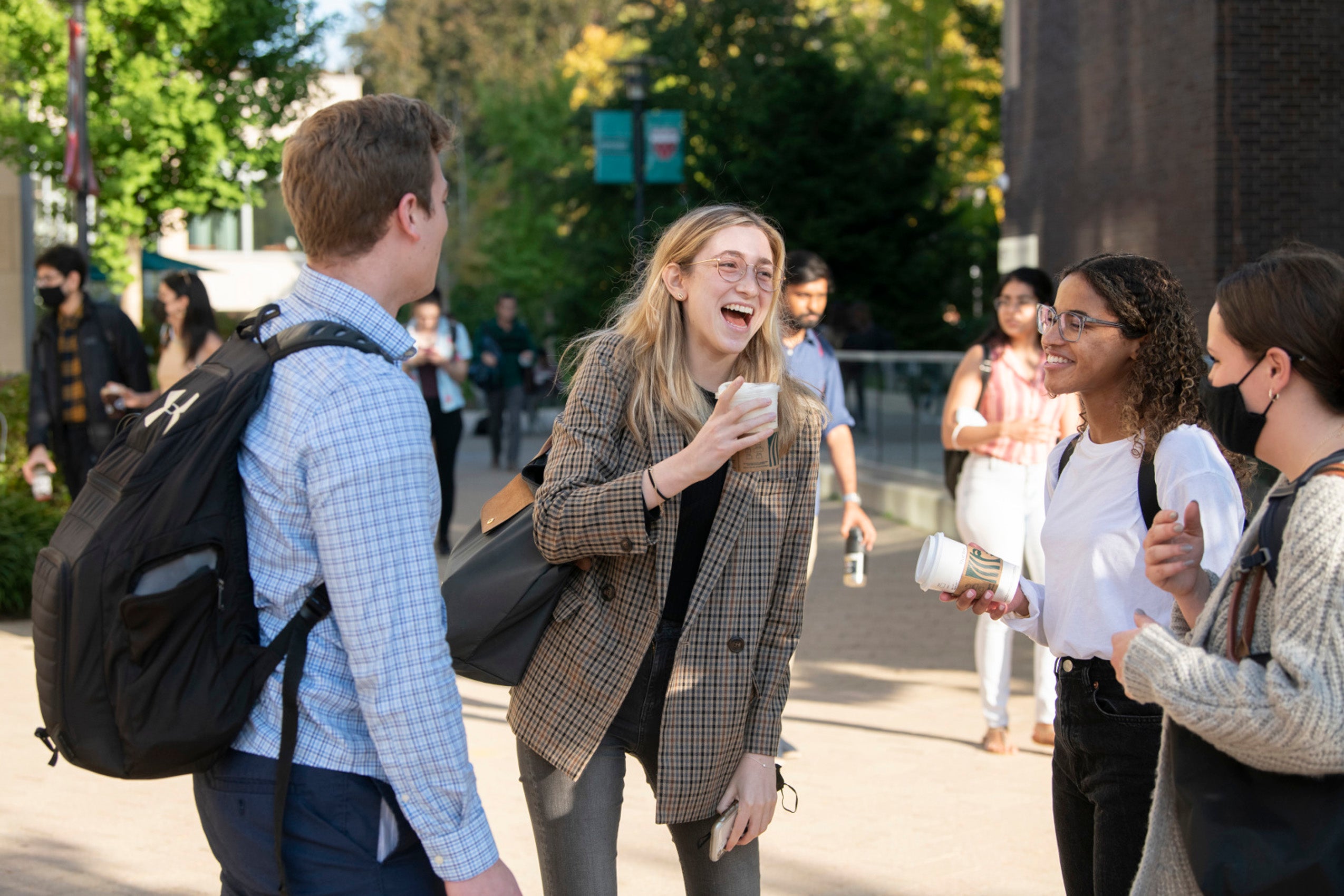 A group of students standing outside on a campus laughing and talking