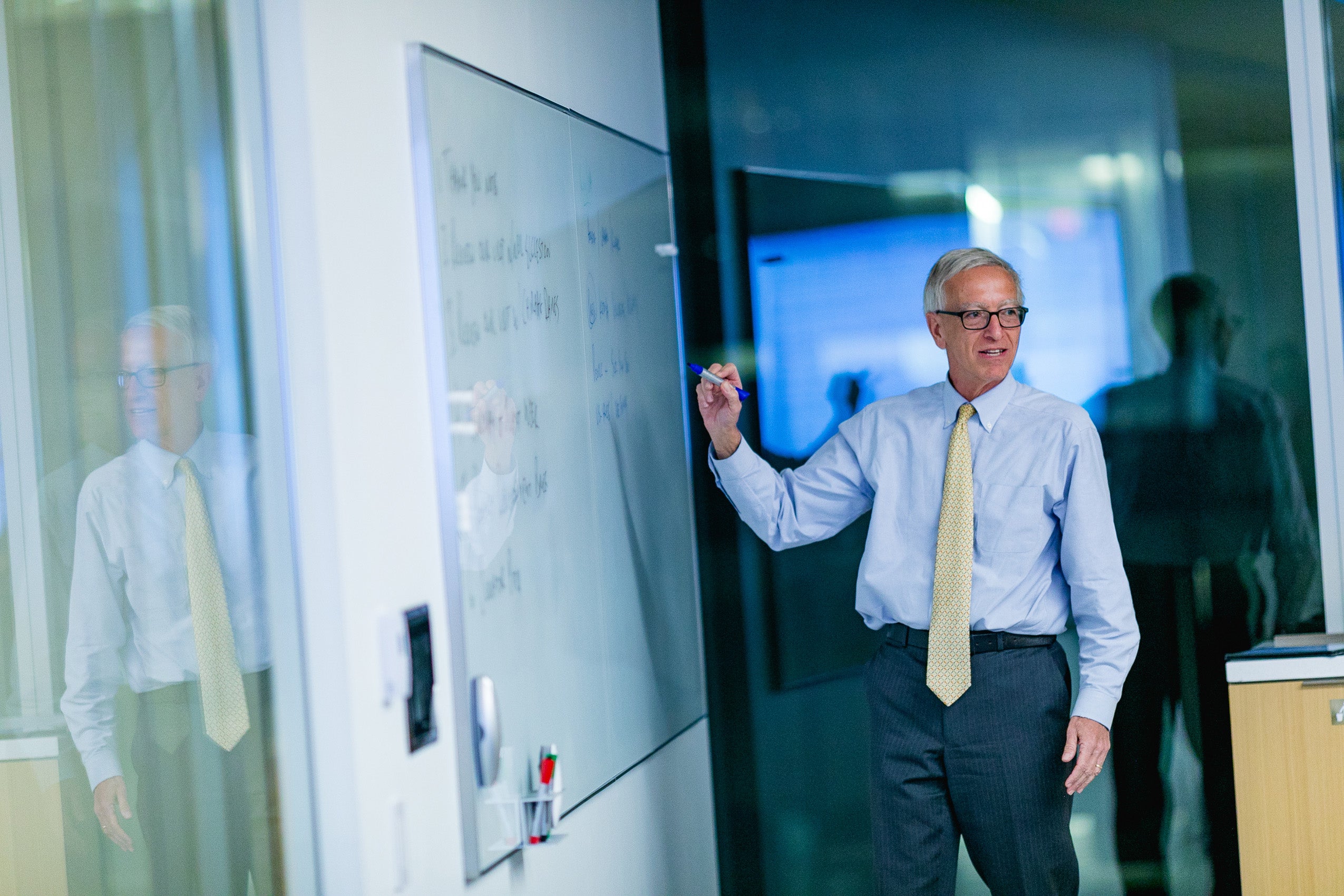 A man turns to others in the room as he makes a point on a white board