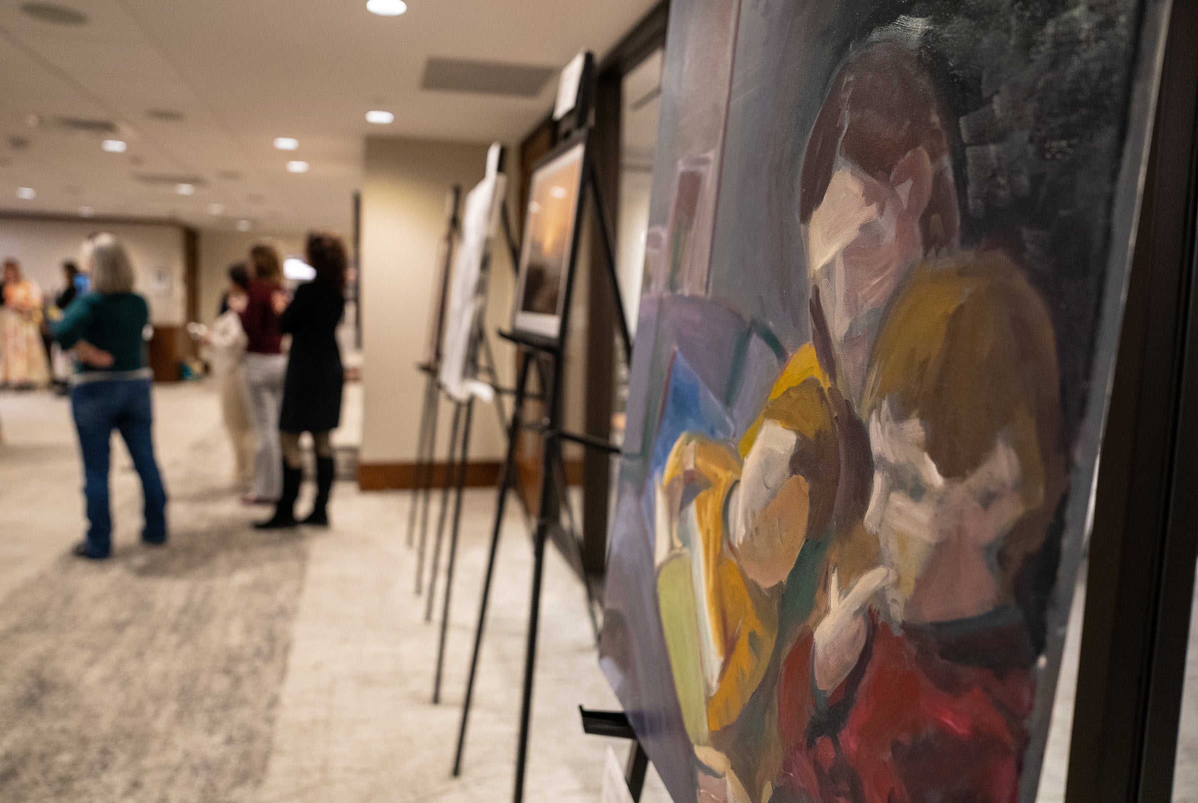 Close up of a painting of three people with people out of focus in the background.