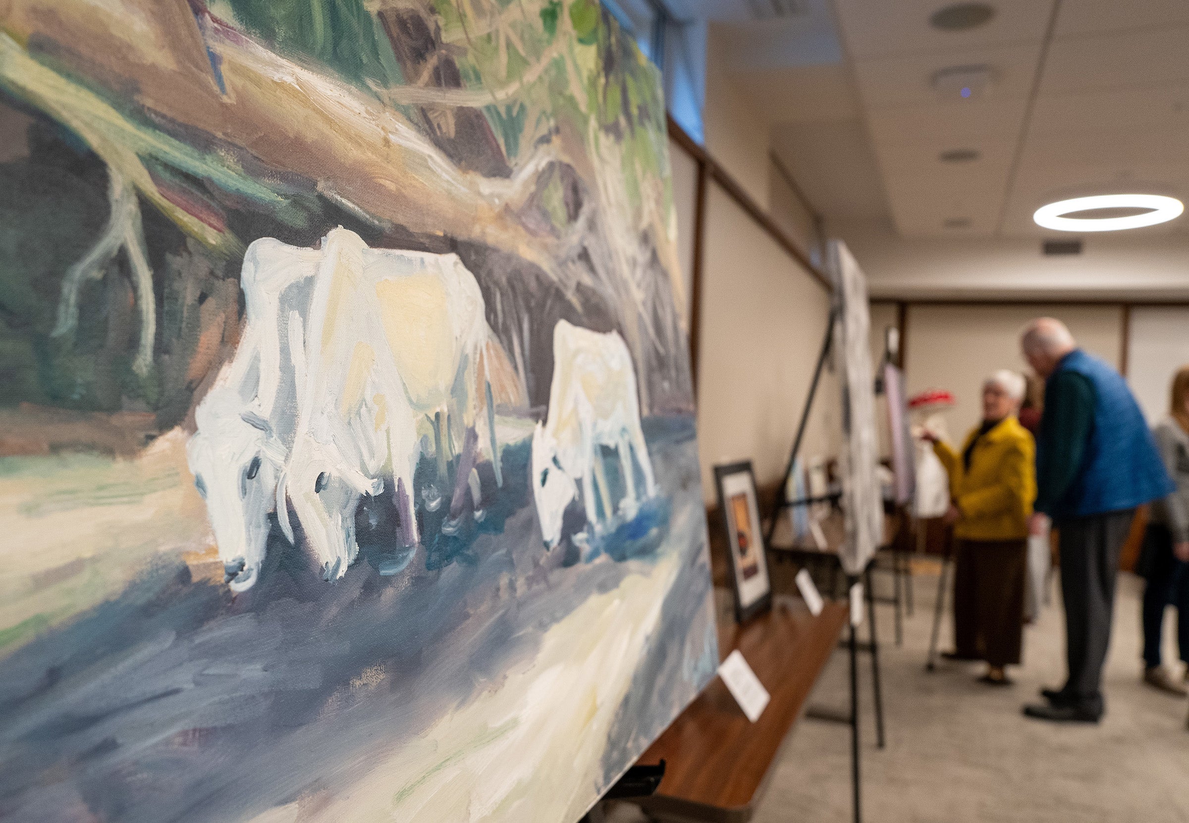 Closeup of a painting of three animals with people out of focus in the background.