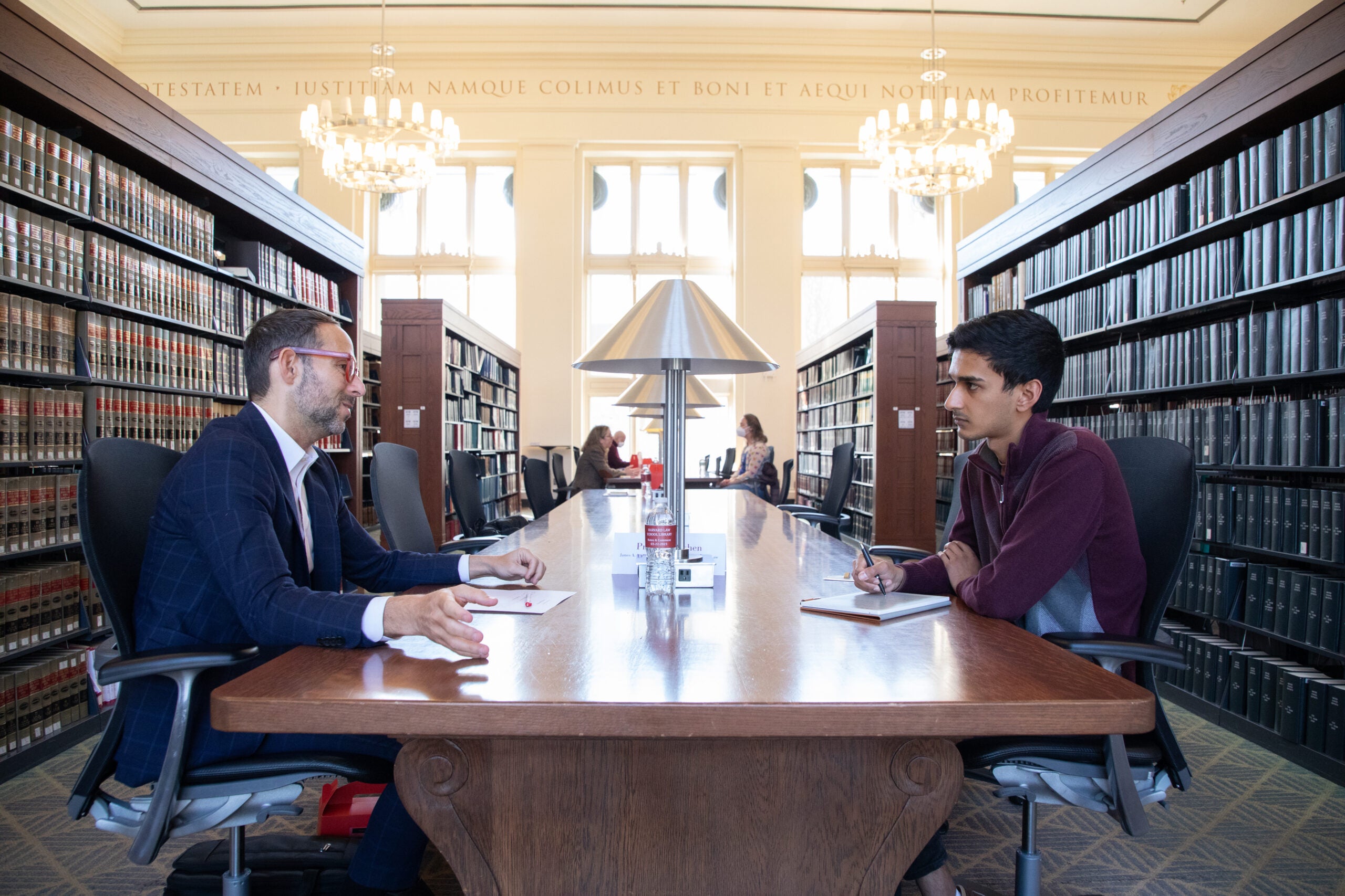 A wide shot of two people conversing in a library at a table