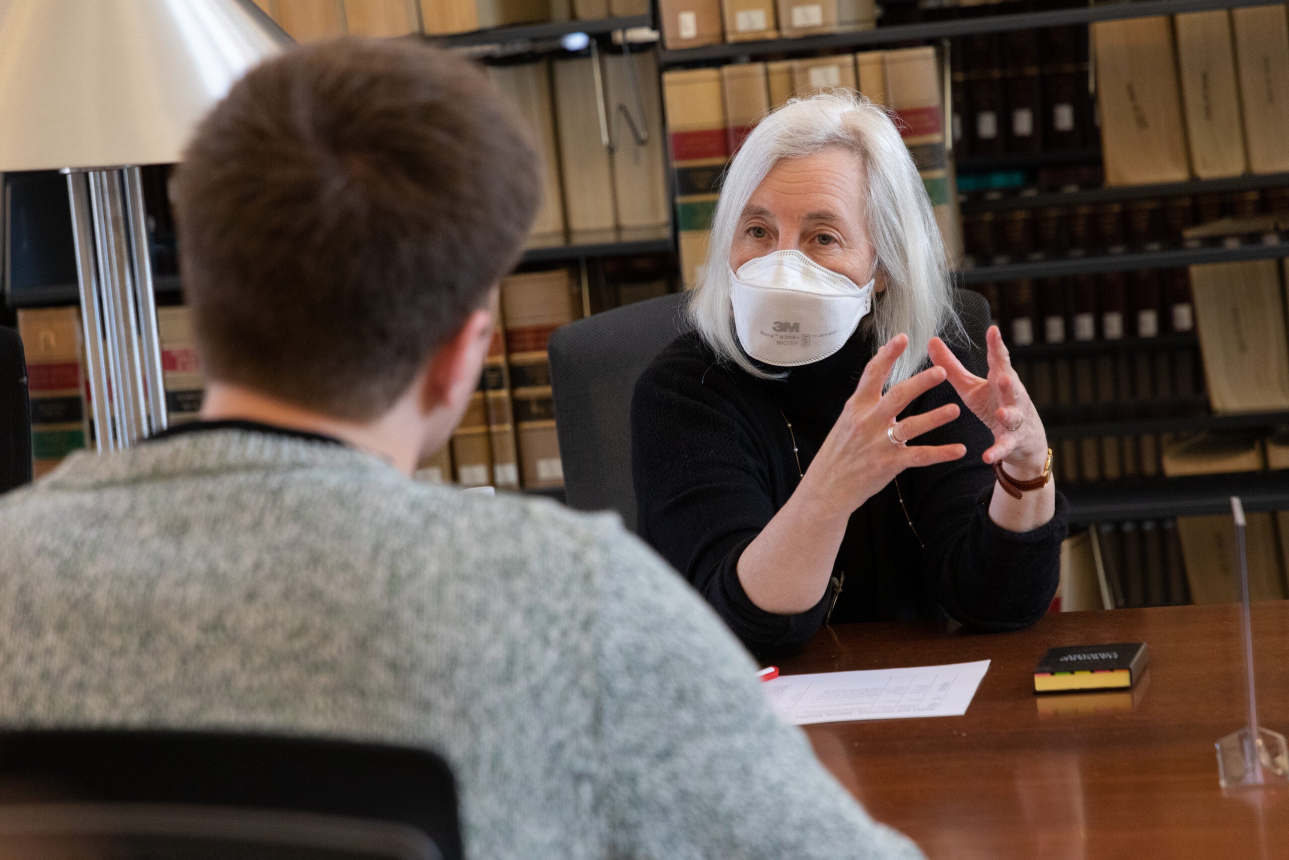 A woman at a table in a library speaking to a man