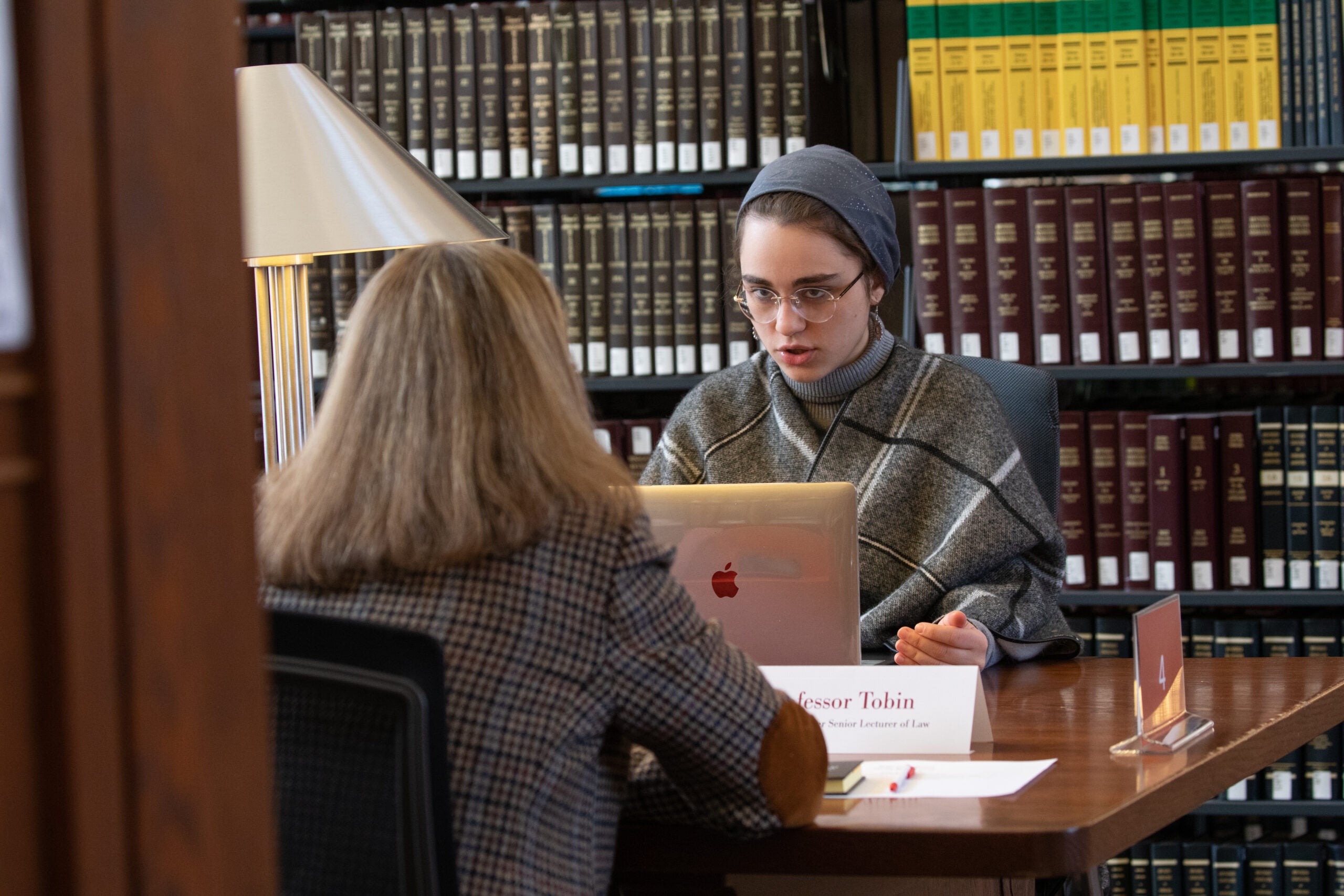 A woman sitting at a table in a library having a conversation with a woman