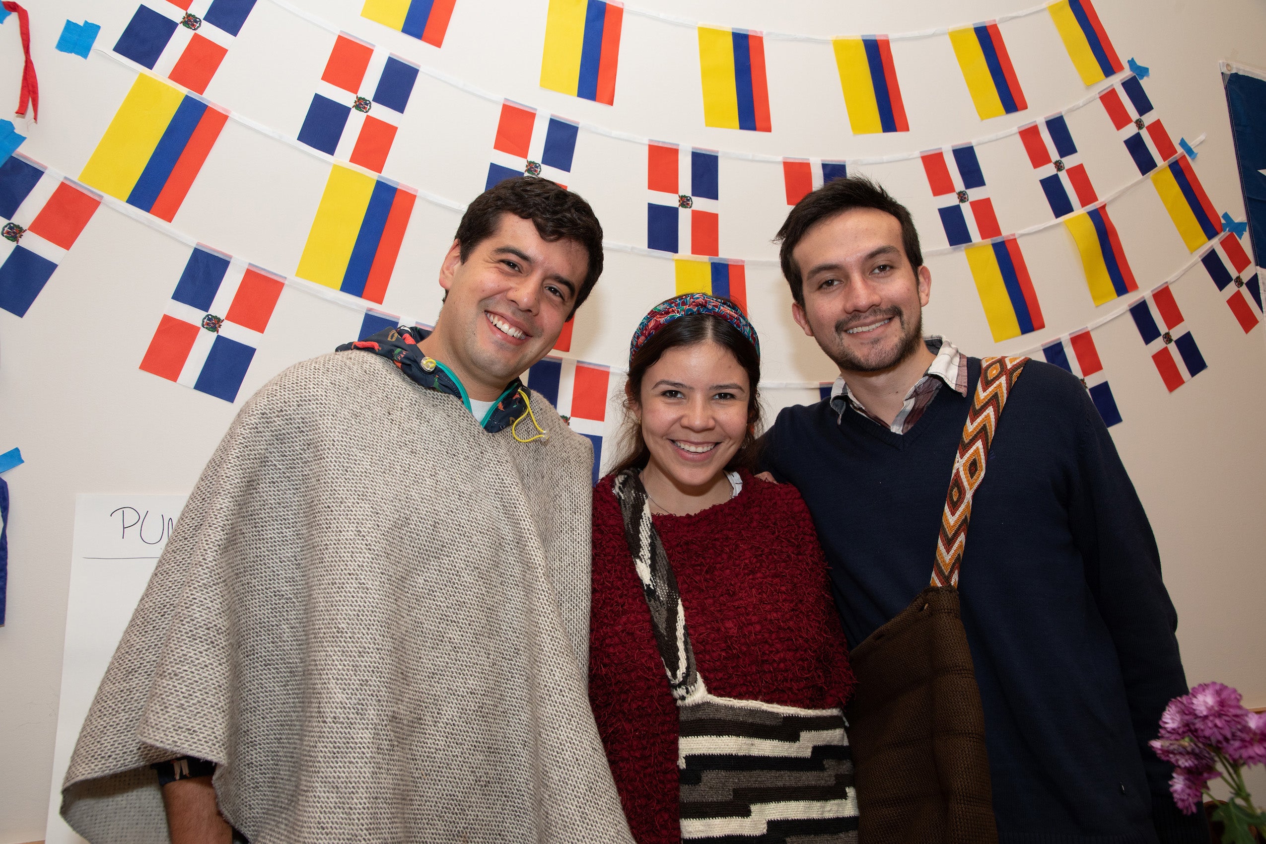 Three people post in front of some flags on the wall