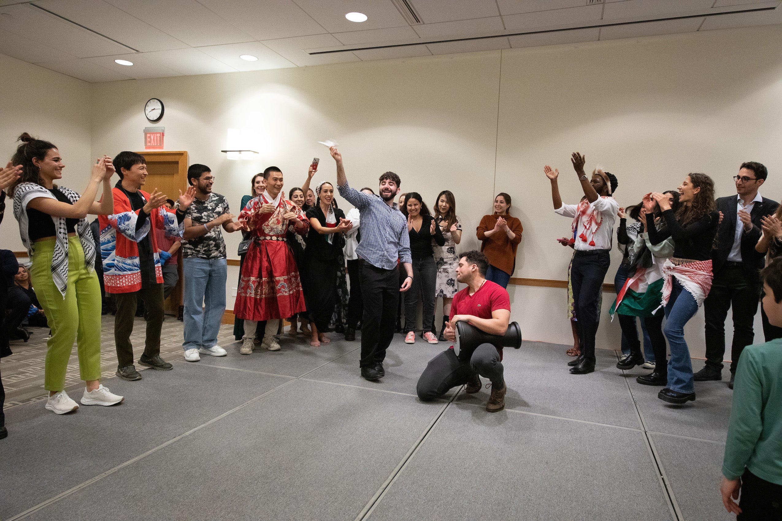 A group of students stand around two men performing in a stage
