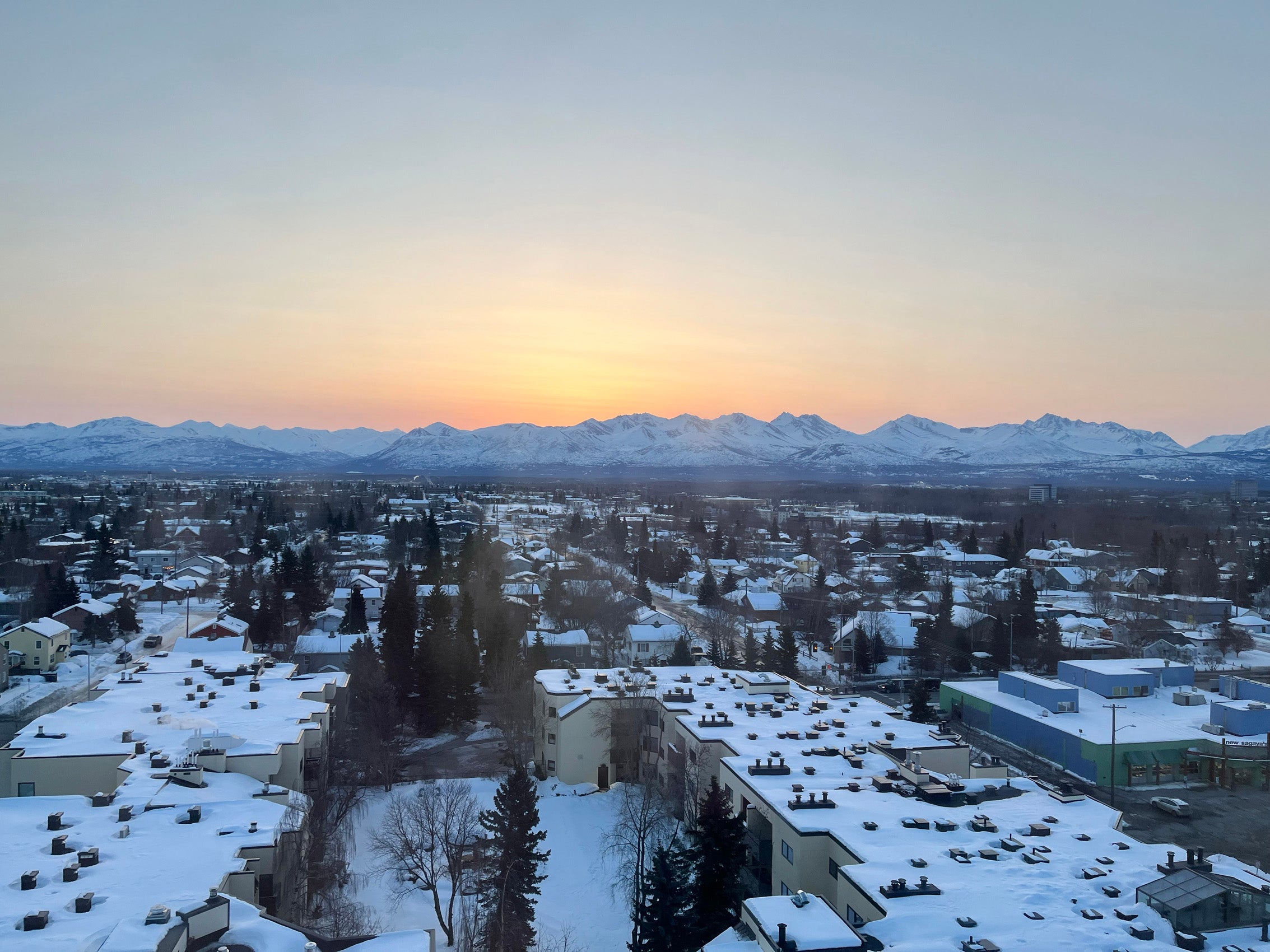 A scene of a snow covered city at sunrise with mountains in the background