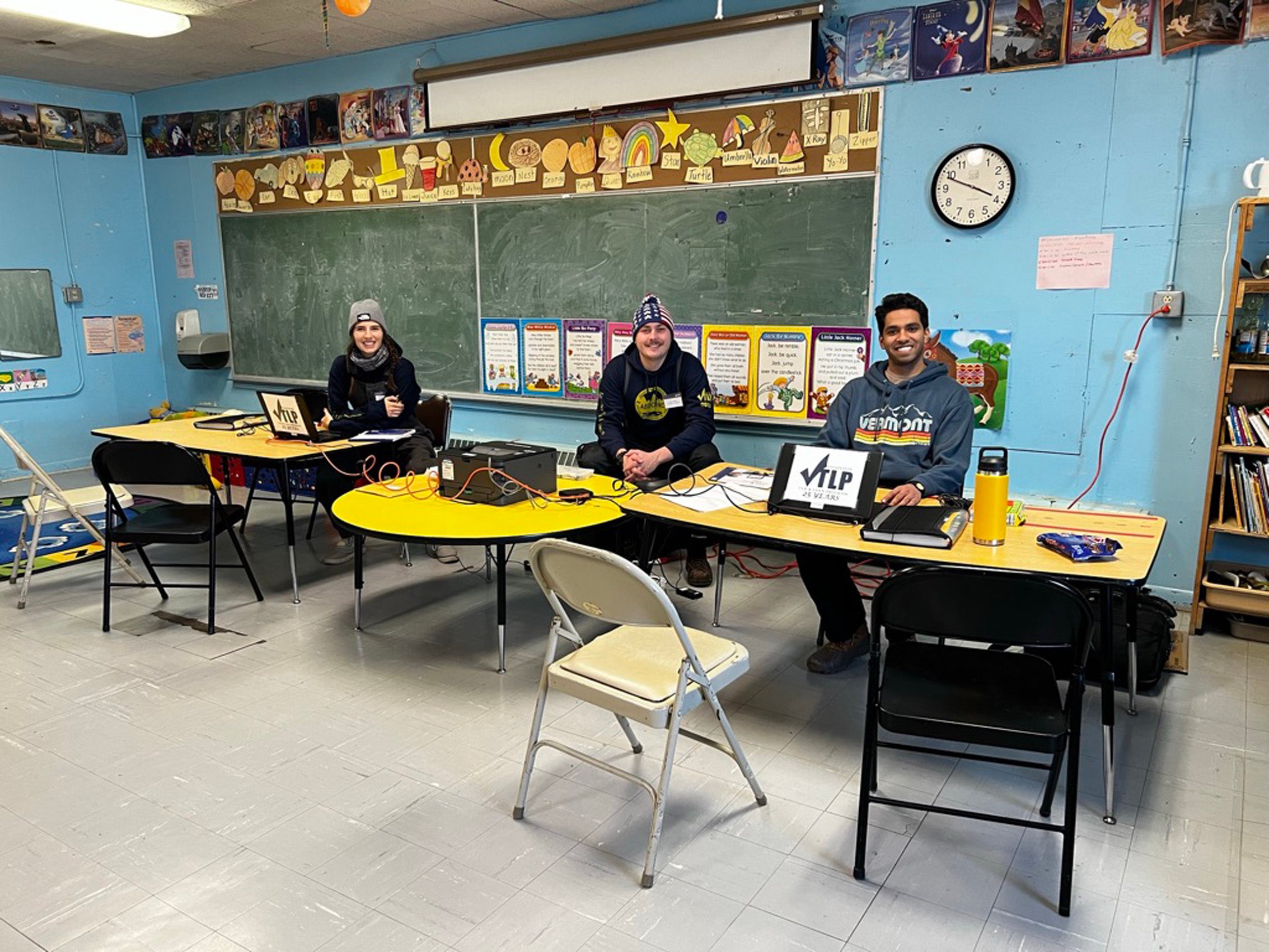 Three individuals sitting at tables behind computers in a classroom