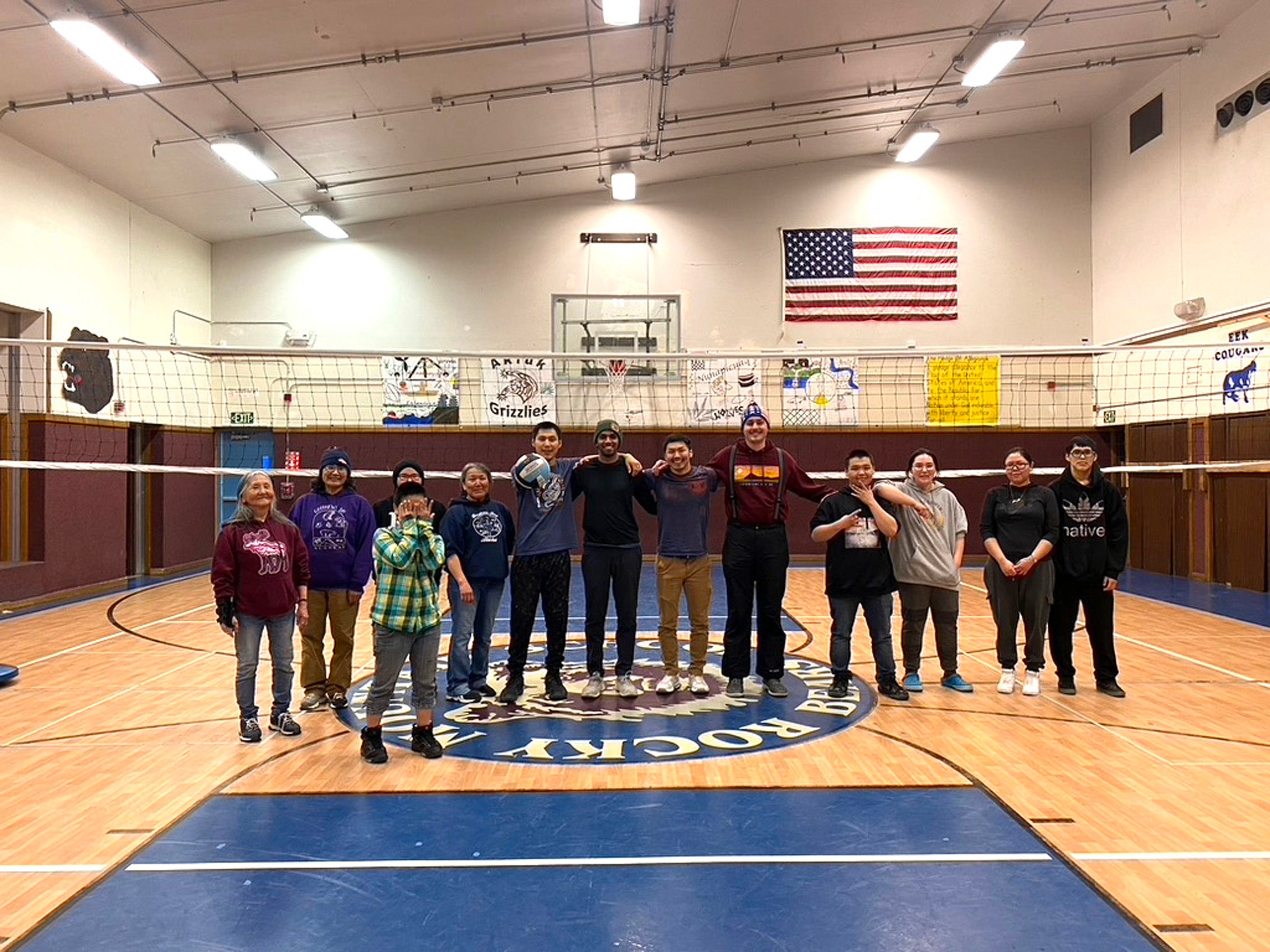 A group of people lines up near a volley ball net in a gym