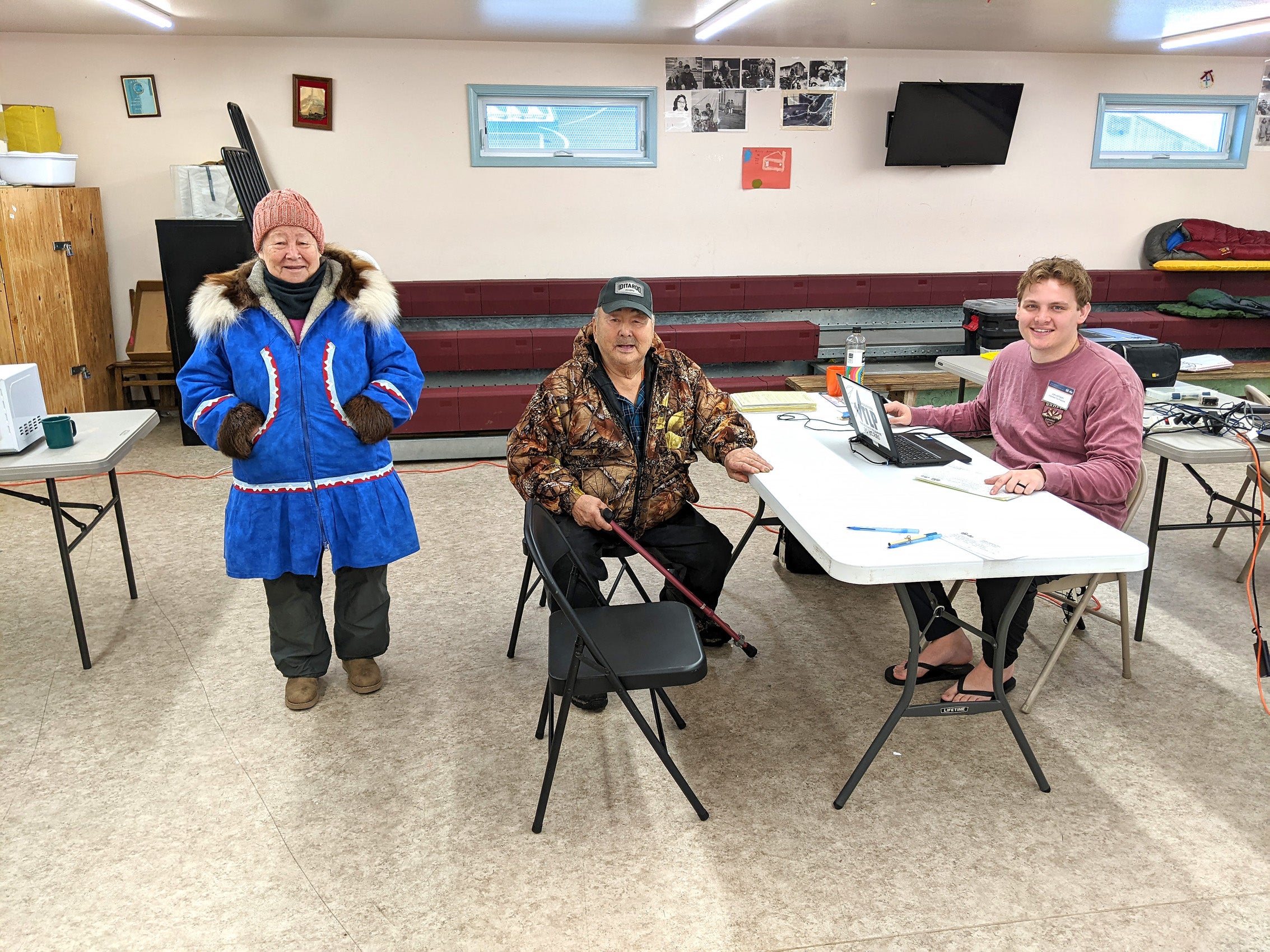 A man sitting behind a computer at a table in a room with two members of the community