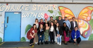 A group of people pose in front of a colorful mural