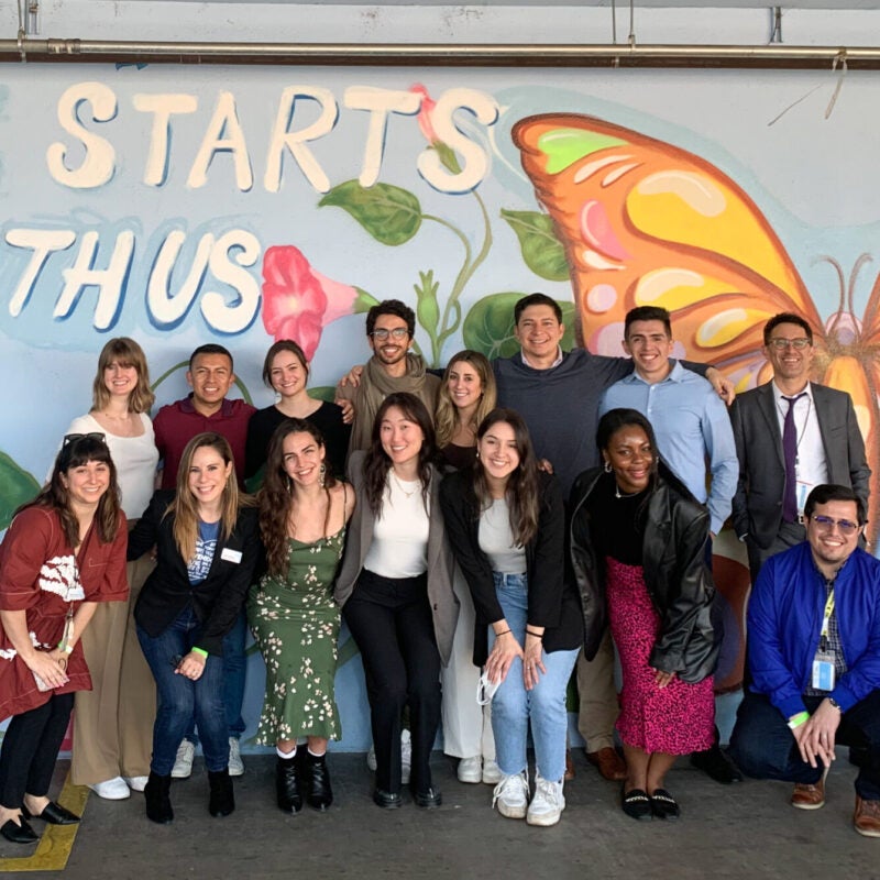 A group of people pose in front of a colorful mural