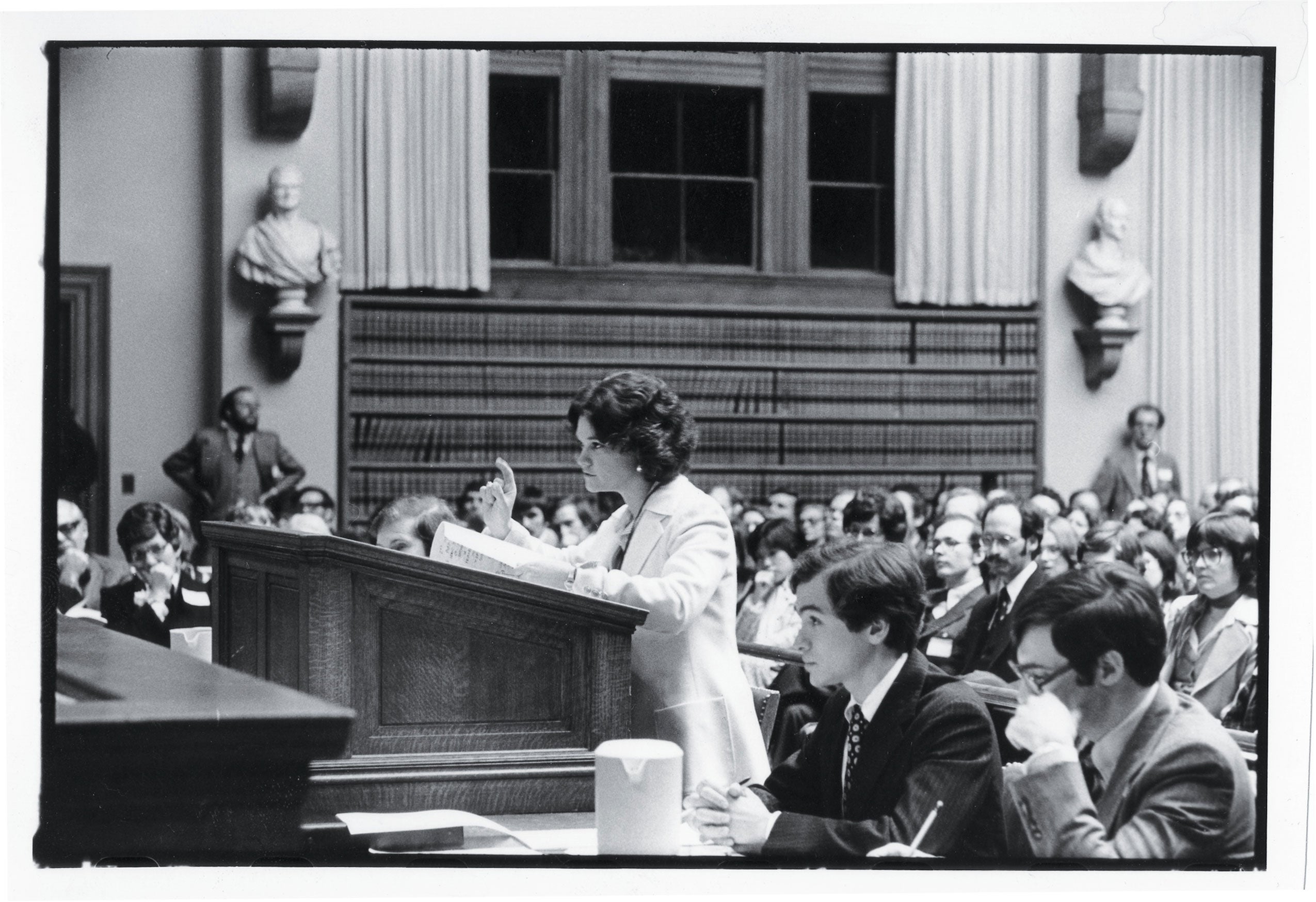 A woman standing at a podium making a point in a room filled with people