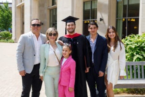 A student in graduation cap and gown poses with his family outside a building on the Harvard Law School campus.