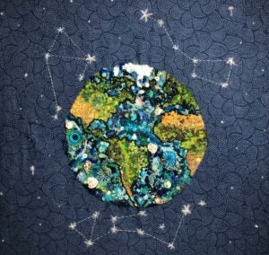 An embroidered depiction of the earth and constellations against a blue background.