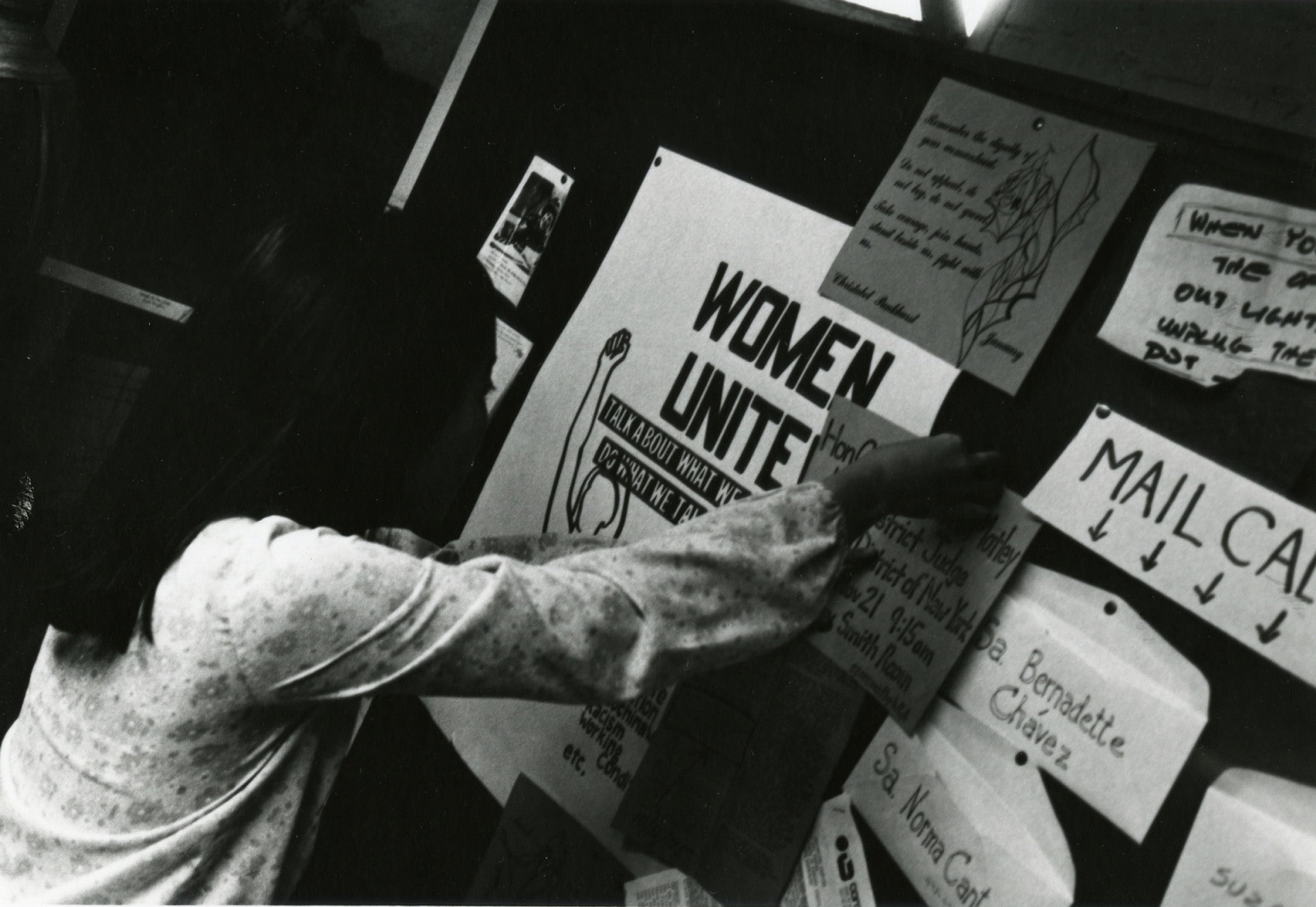 A woman puts up a sign on a bulletin board large sign on the board says Women Unite