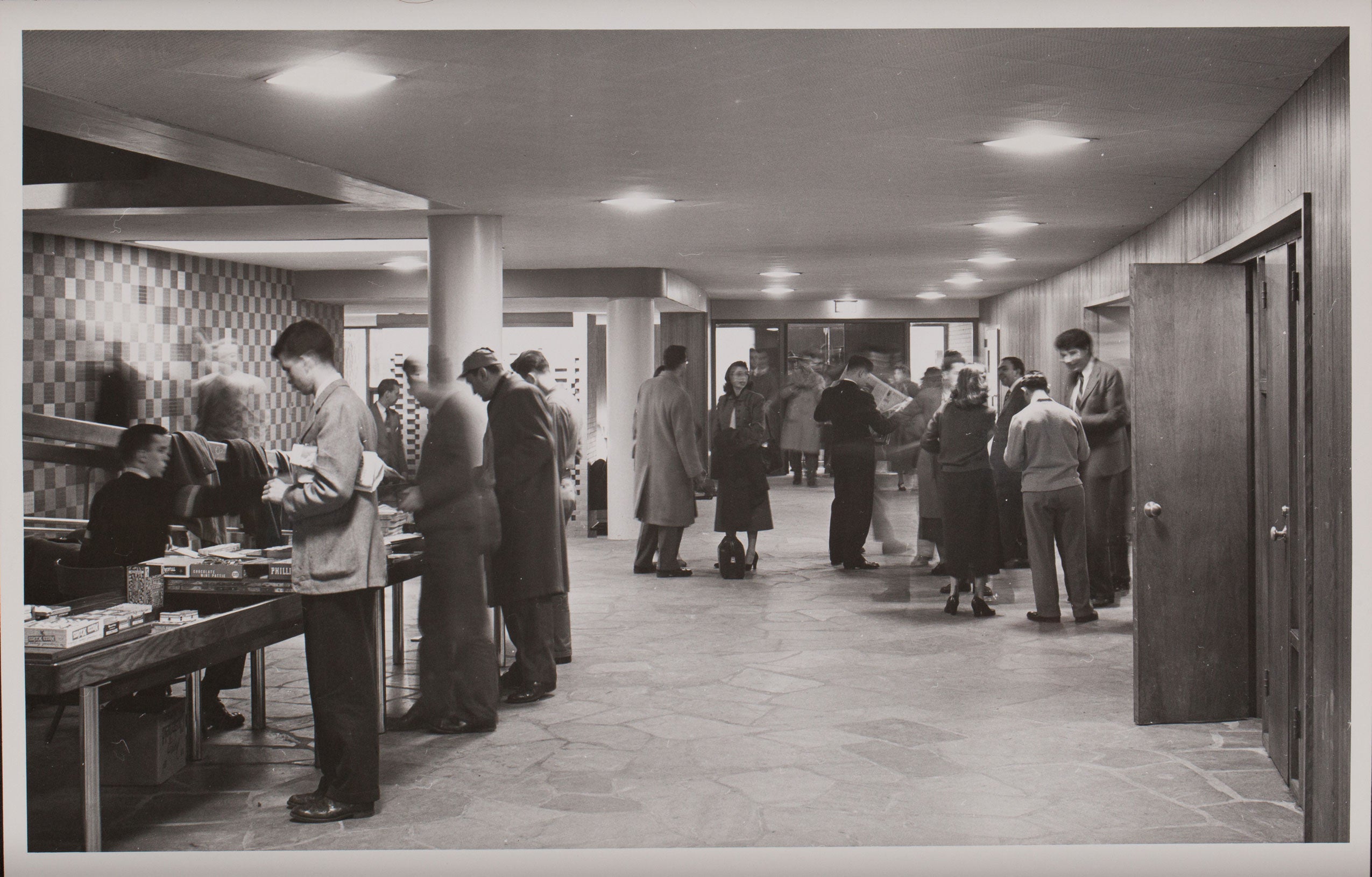 Black and white photo of students buying books, chatting in the hallway of a campus building