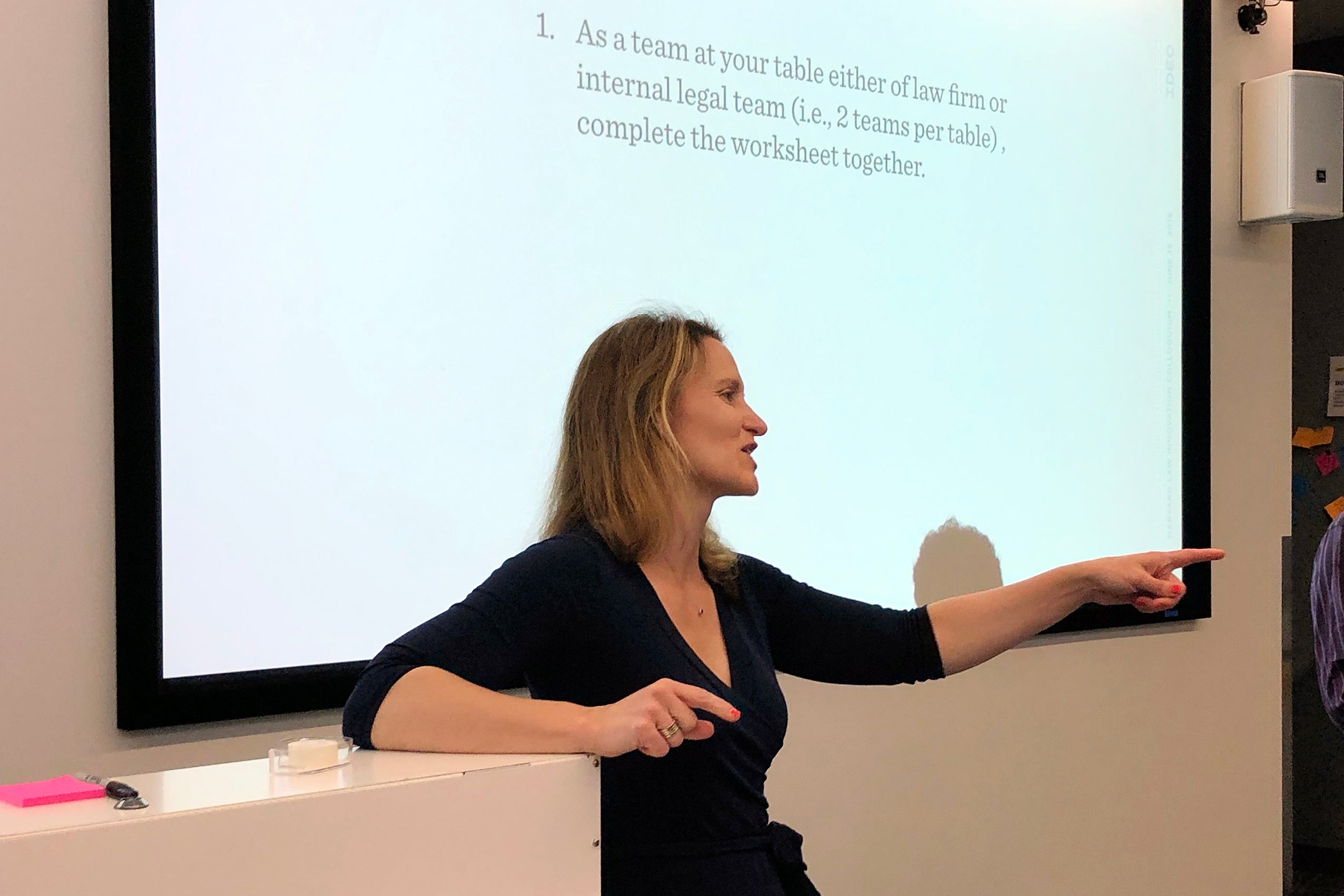 Woman speaking in front of a screen leading a group of people