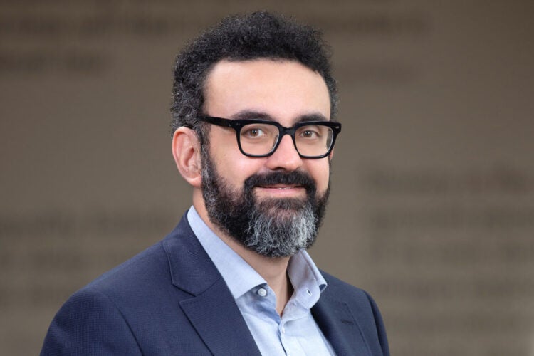 Man wearing a blue suit in a hallway looking out to the camera