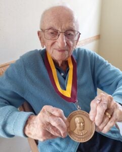 A older man wearing a ribbon with a medal at the end