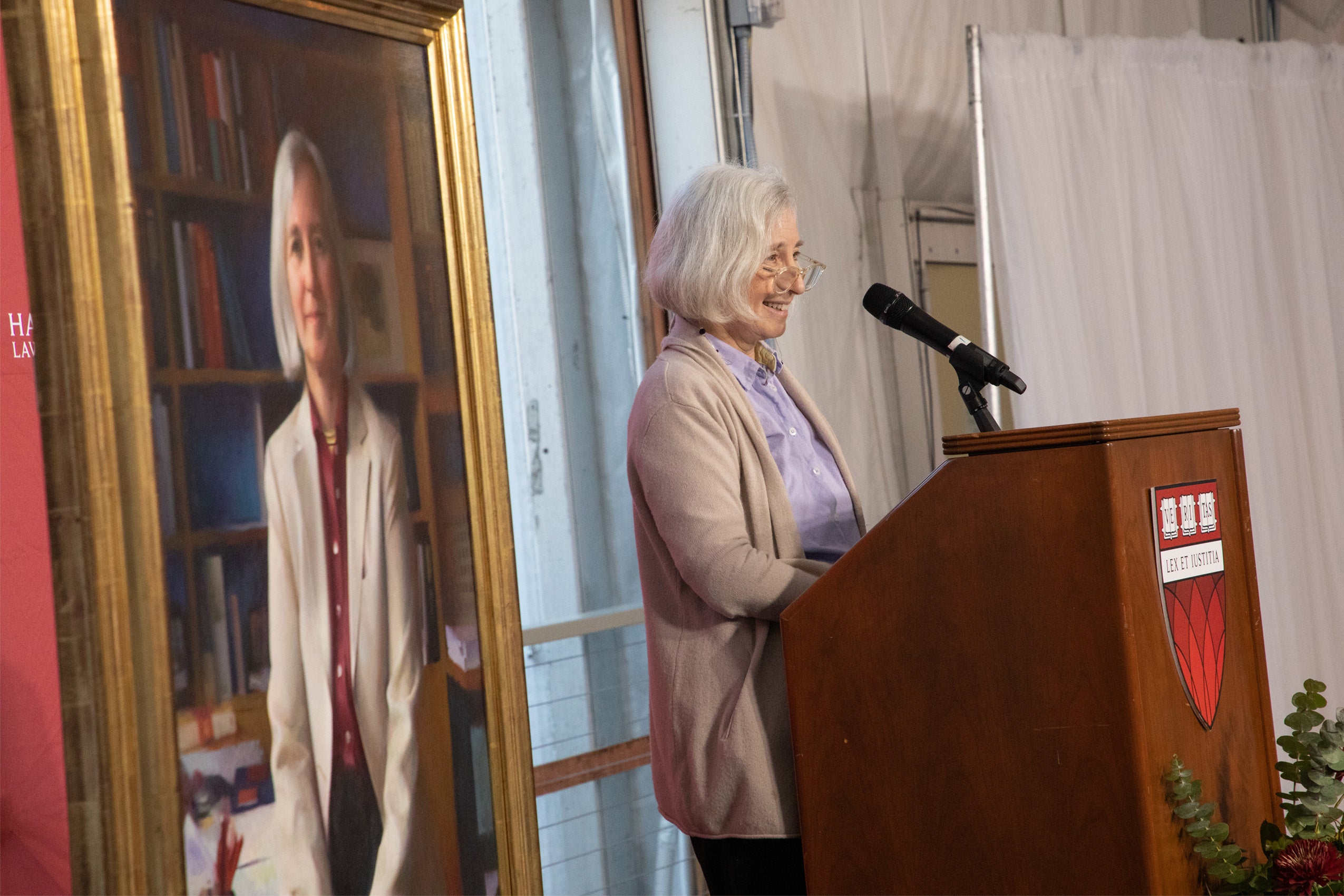 Woman speaks at podium in front of portrait