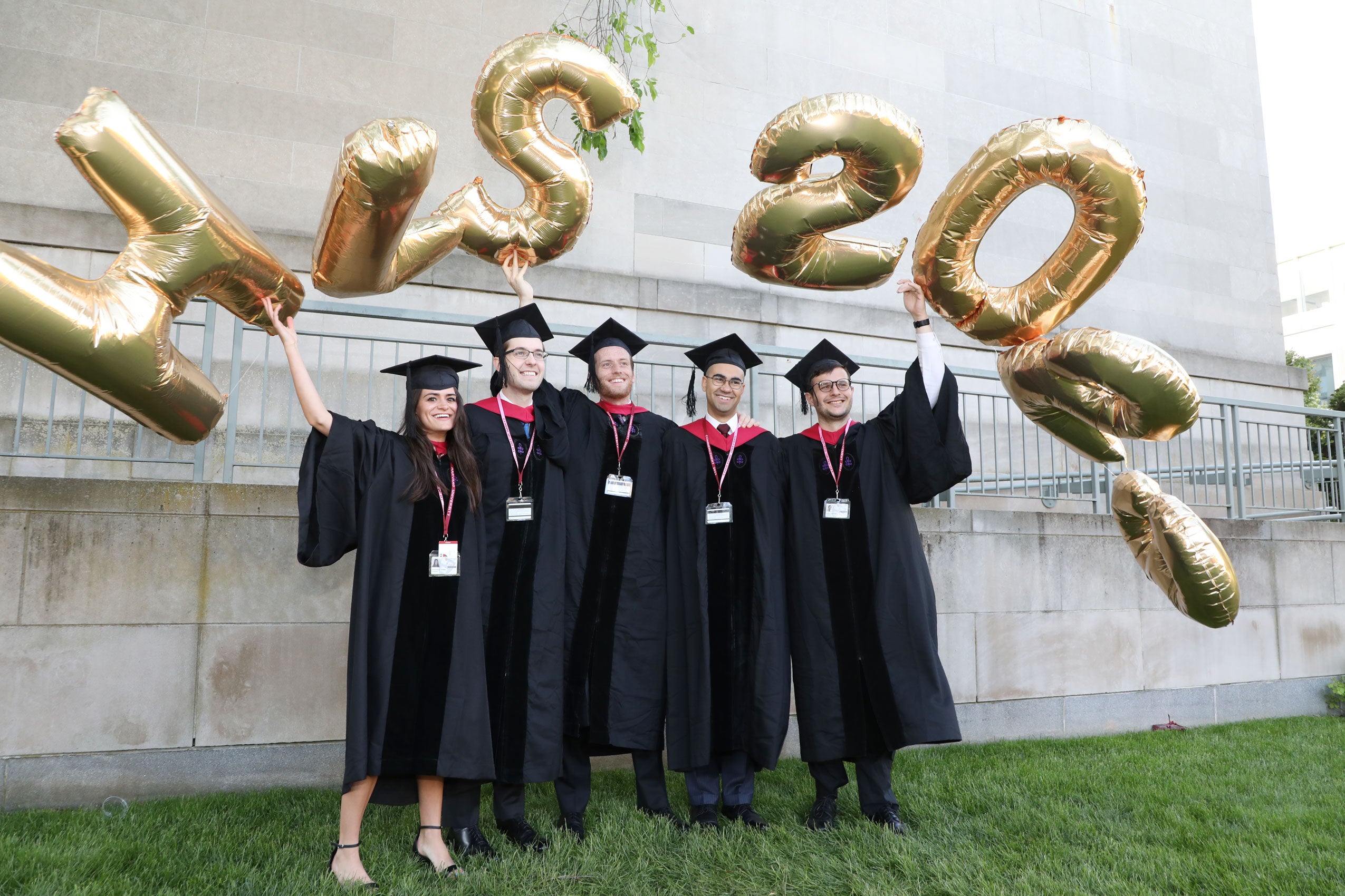 Five grads wearing caps and gowns pose under HLS 2023 balloons