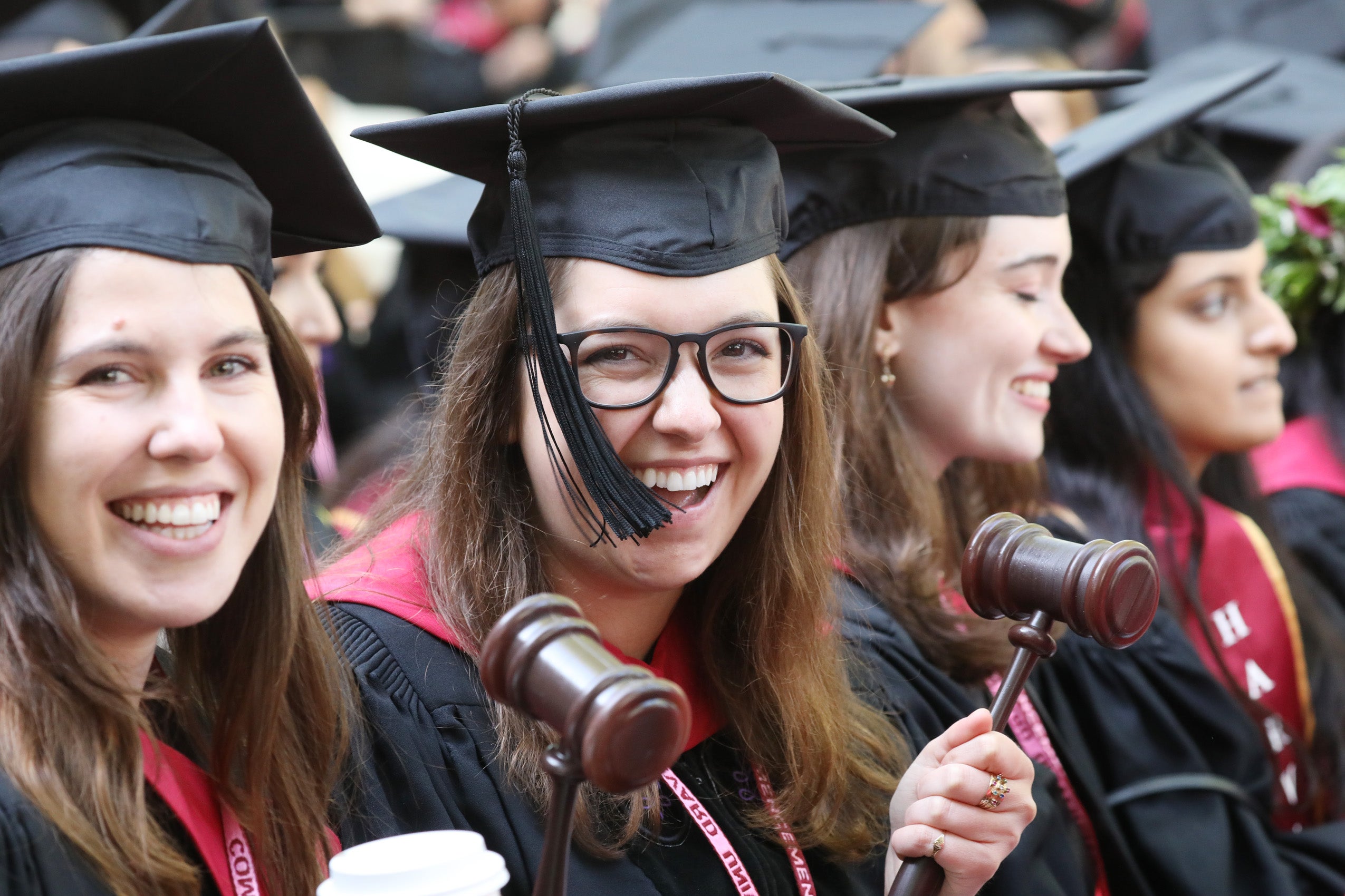 Grads holding gavels smile from the audience at commencement
