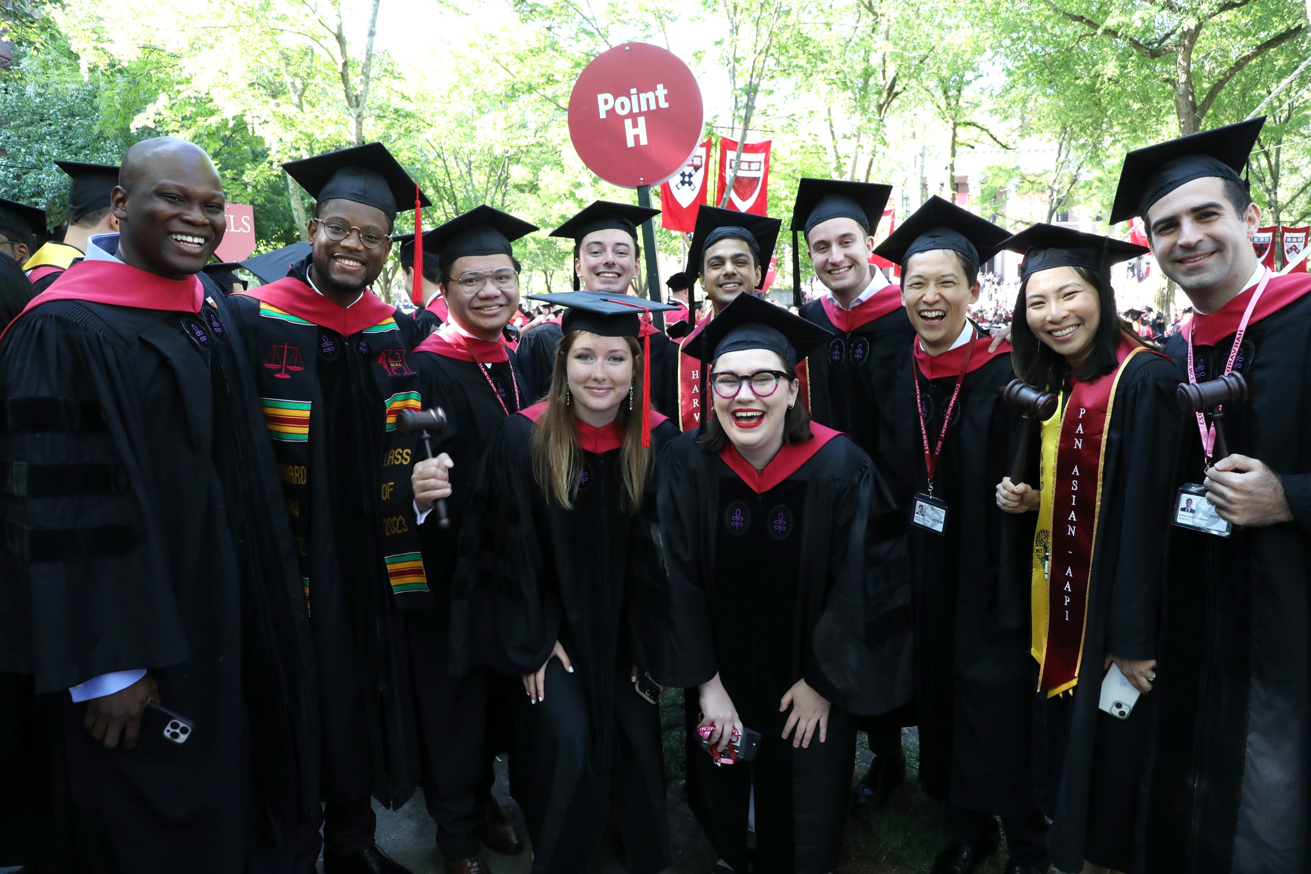 Group of students pose together in regalia holding Point H sign