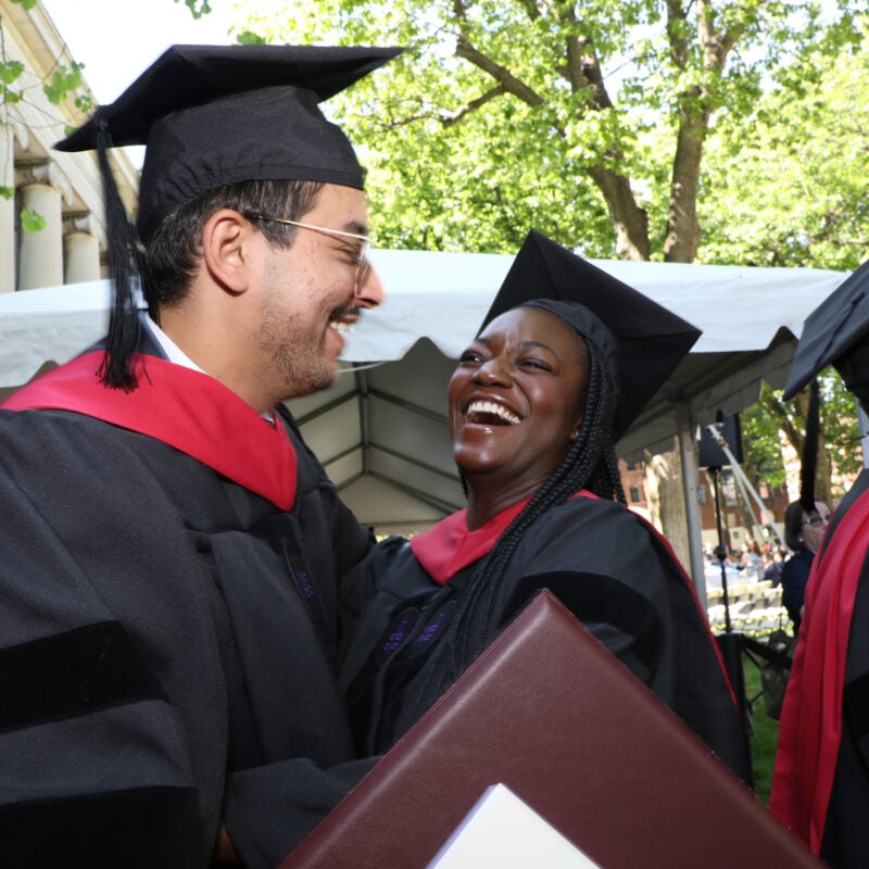 A man in a cap and gown and a woman in a cap and gown share a light moment