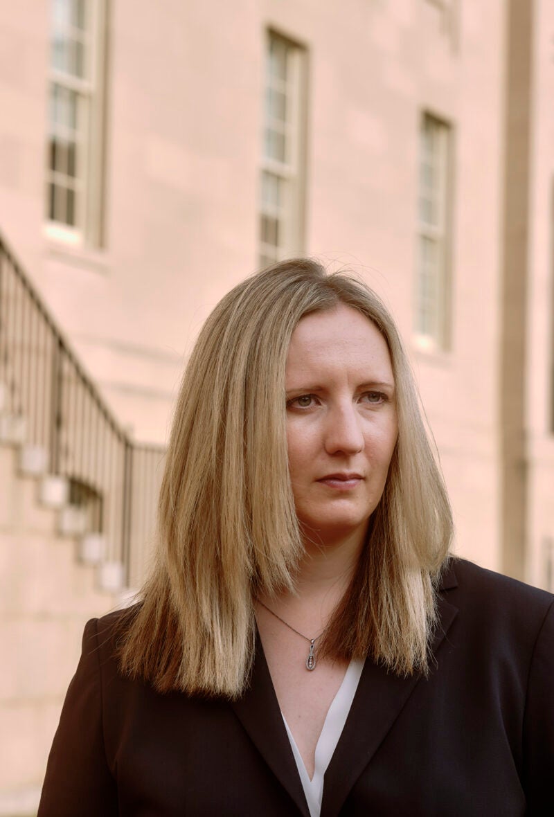Woman standing outside a beige building looking pensive.