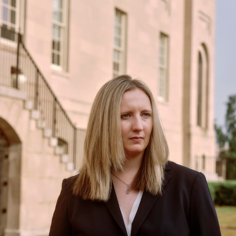 Woman standing outside a beige building looking pensive.