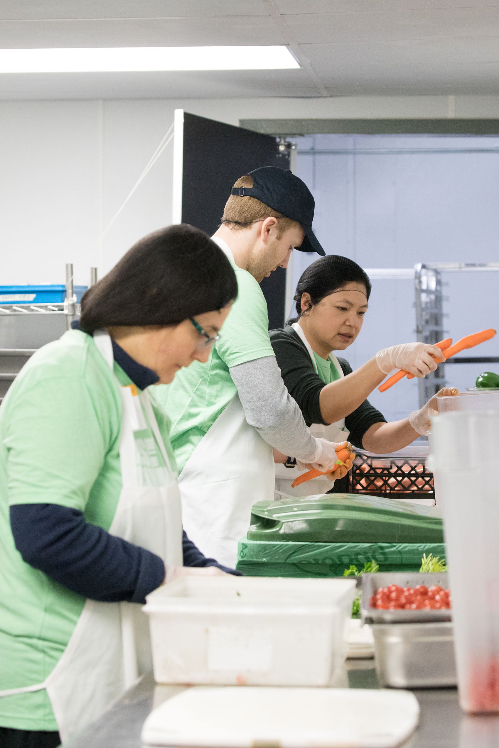 group of people working in a kitchen with carrots and tomatoes