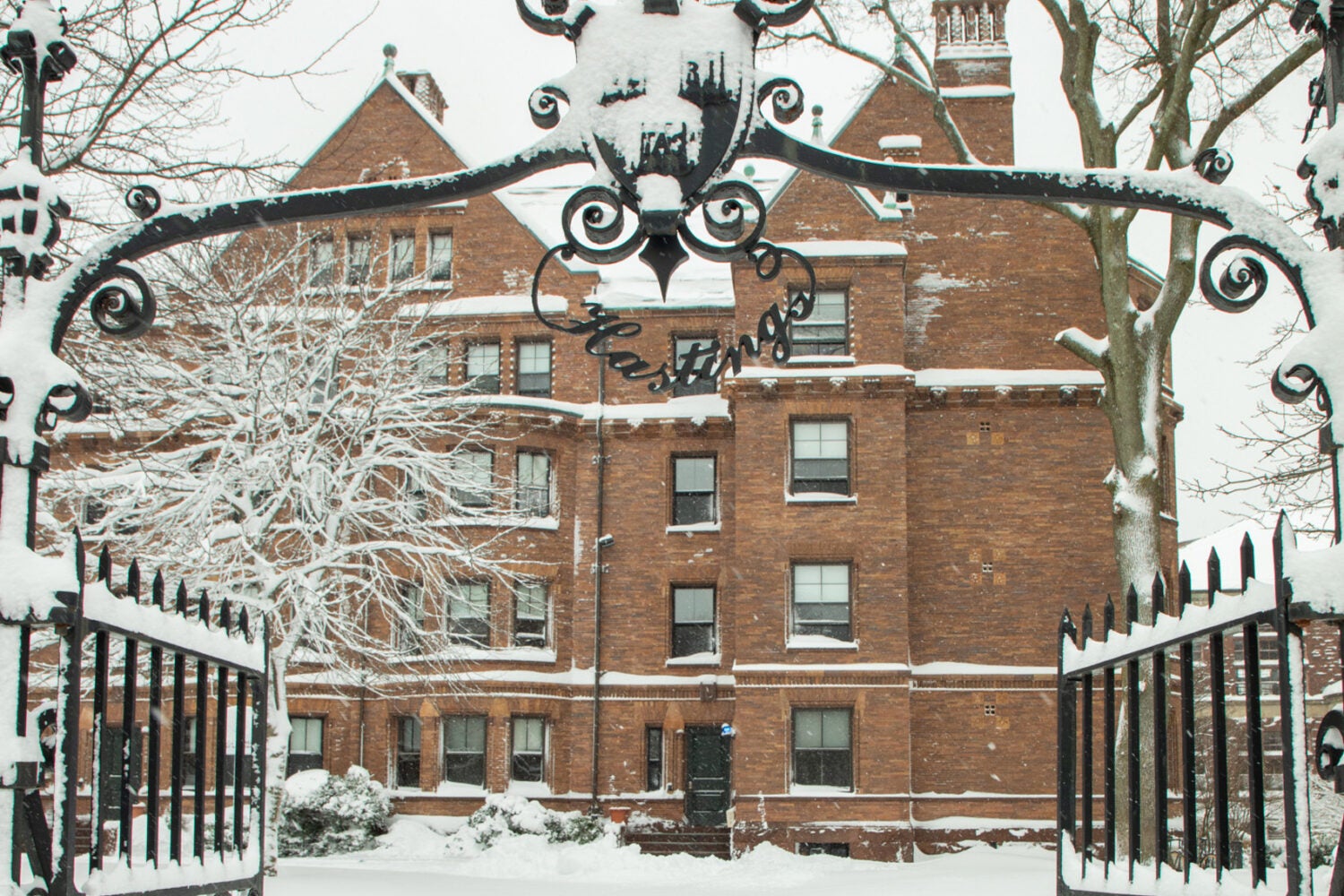 A red brick snow covered building sits behind black iron gates