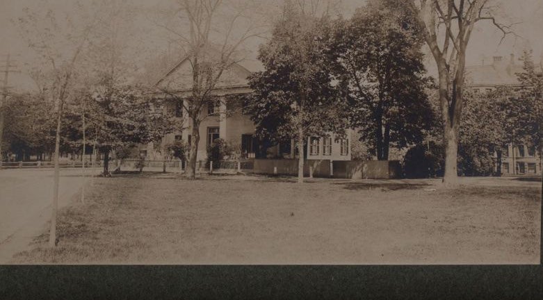 A white house with columns near a grassy law with trees