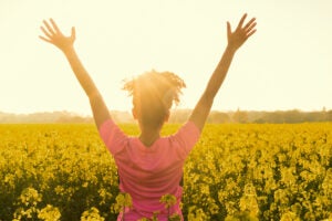 young woman celebrating in field of yellow flowers.