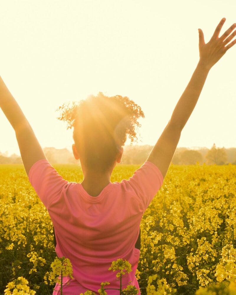 young woman celebrating in field of yellow flowers.