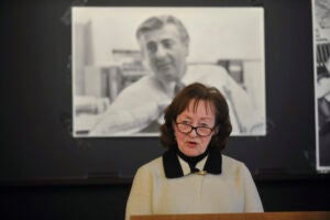 A woman speaking at a podium in front of a black and whit photograph of a man