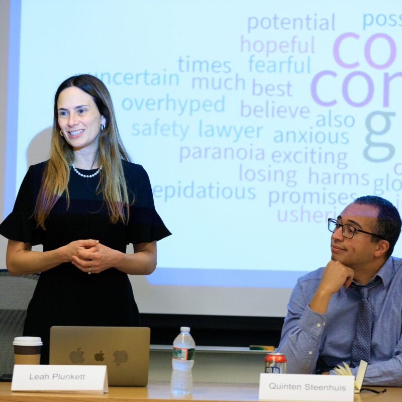 a woman stands in front of a projector screen, a man sits next to her